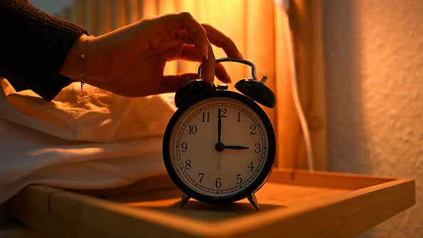 A woman reaches for an alarm clock next to her bed. 