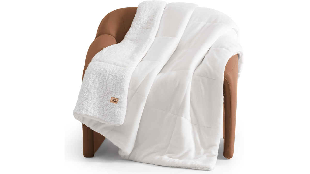 White UGG sherpa-lined quilted throw blanket draped over a tan leather armchair