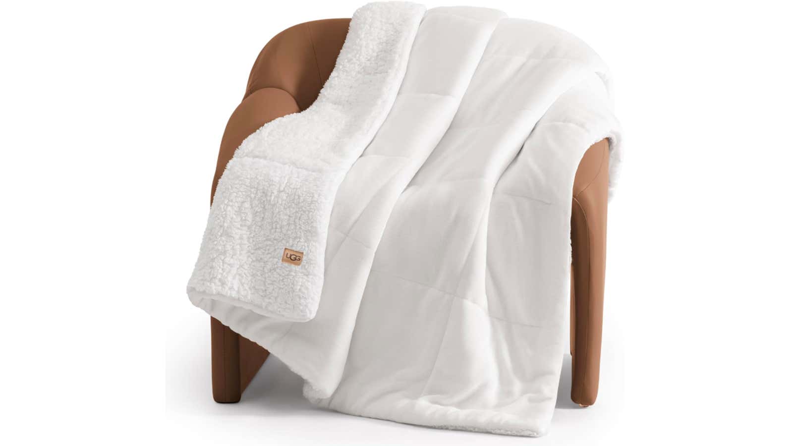 White UGG sherpa-lined quilted throw blanket draped over a tan leather armchair
