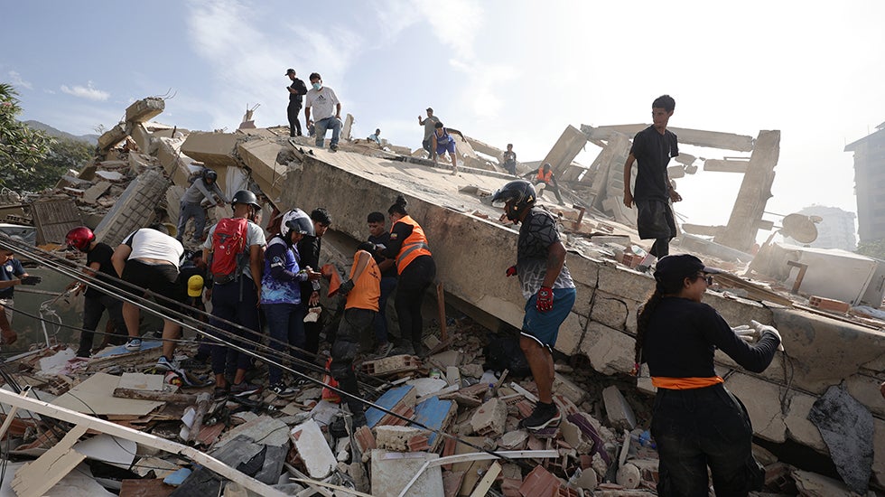 People and rescuers search for victims amid debris of demolished buildings