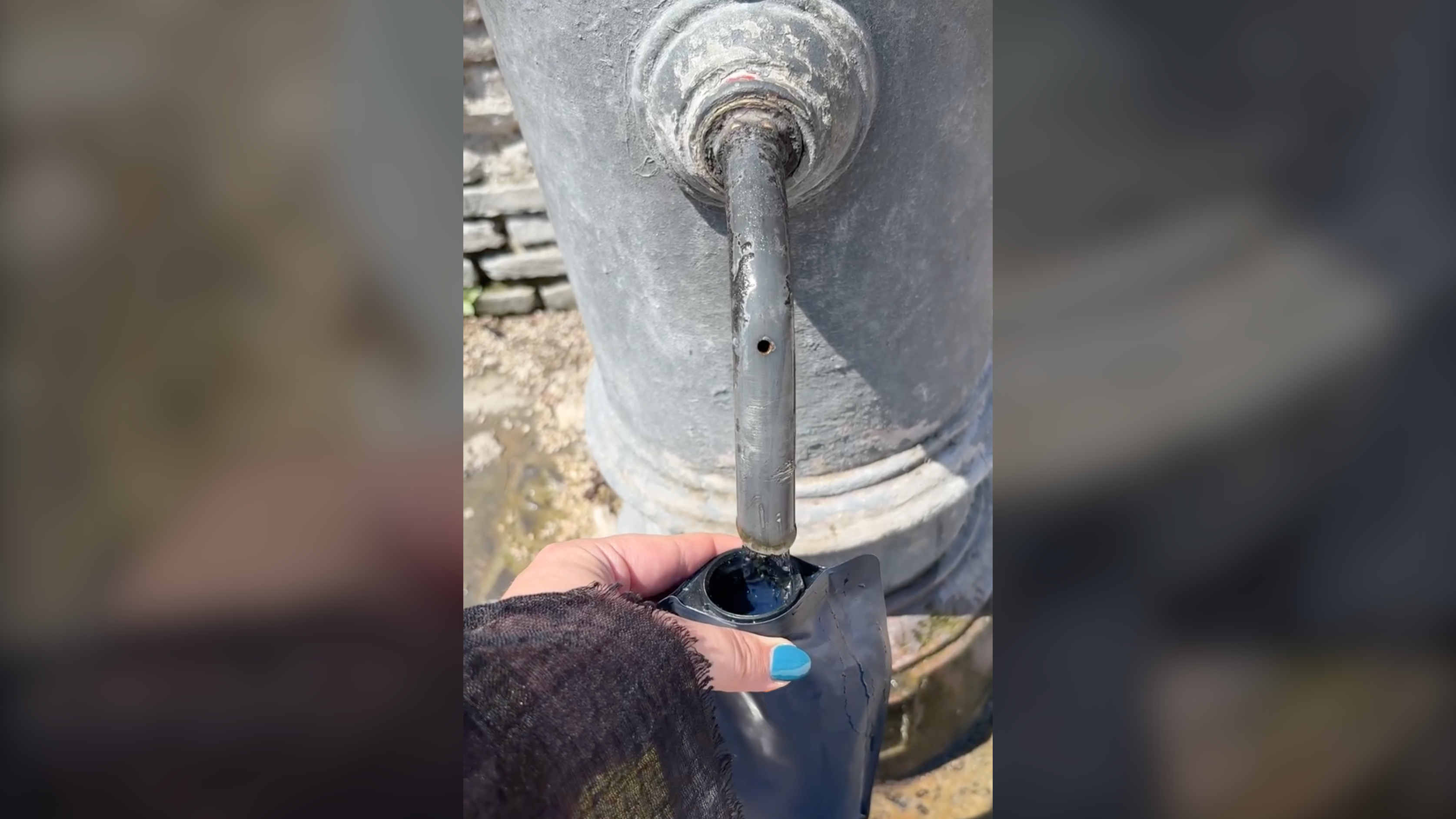 Hand with blue nail polish filling a water bottle from a nasoni water fountain in Rome, Italy