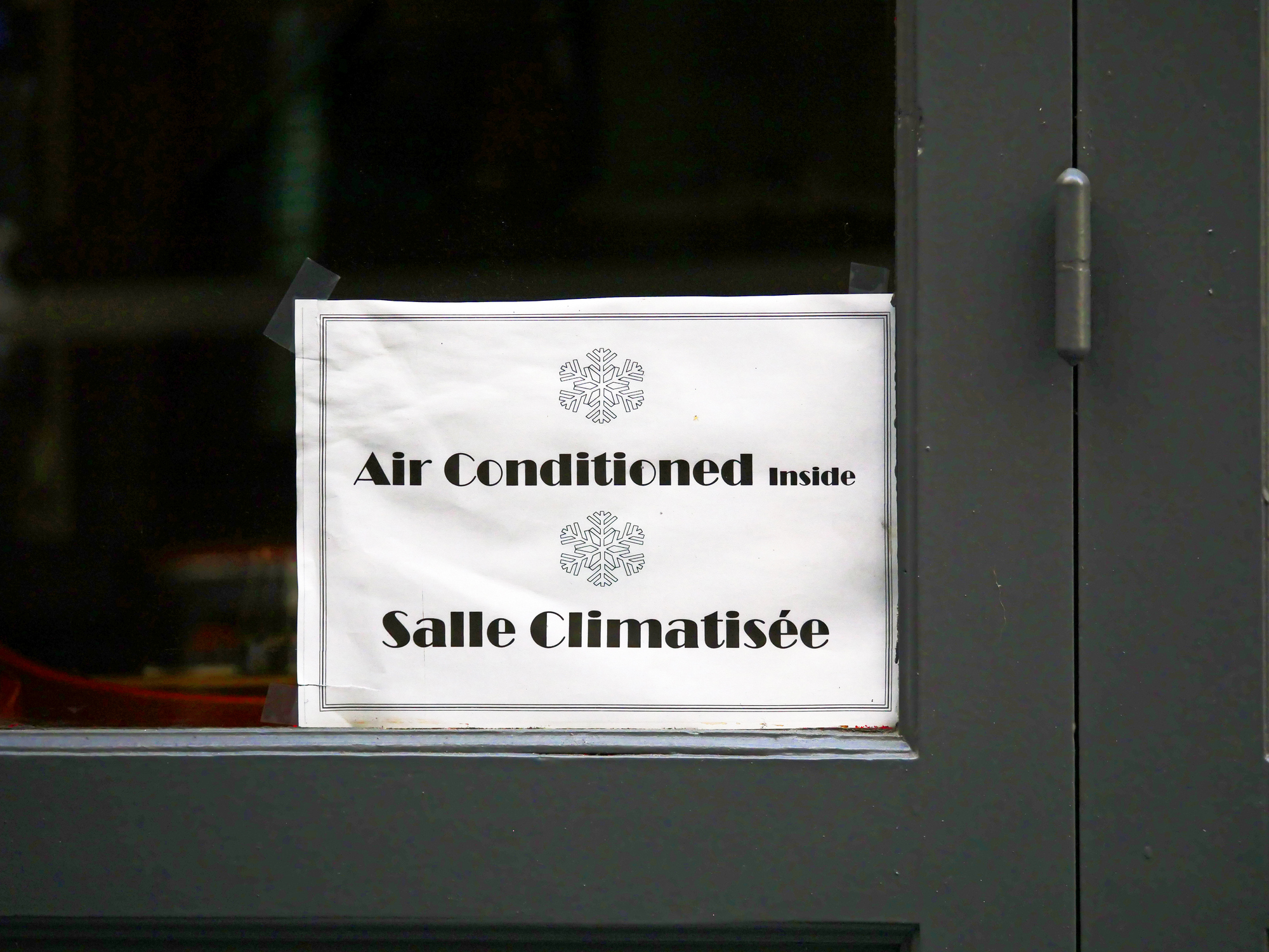 A poster in French and English on the front door of a Parisian restaurant announces that the place is air-conditioned - stock photo
