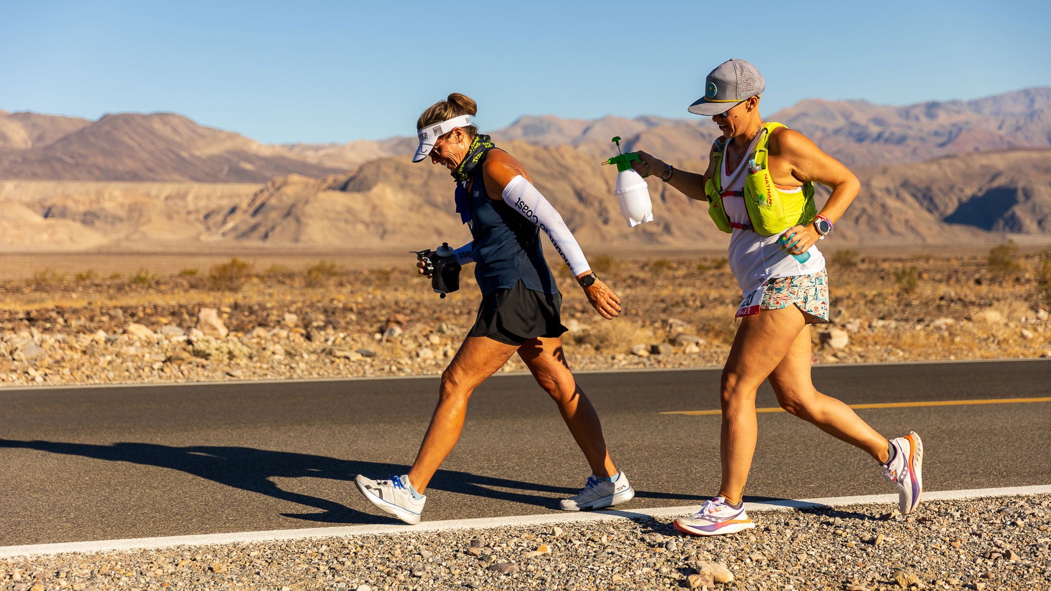A participant in the 2025 Badwater 135 Ultramarathon with her pacer following behind to provide a cooling water spray to support her in the race.