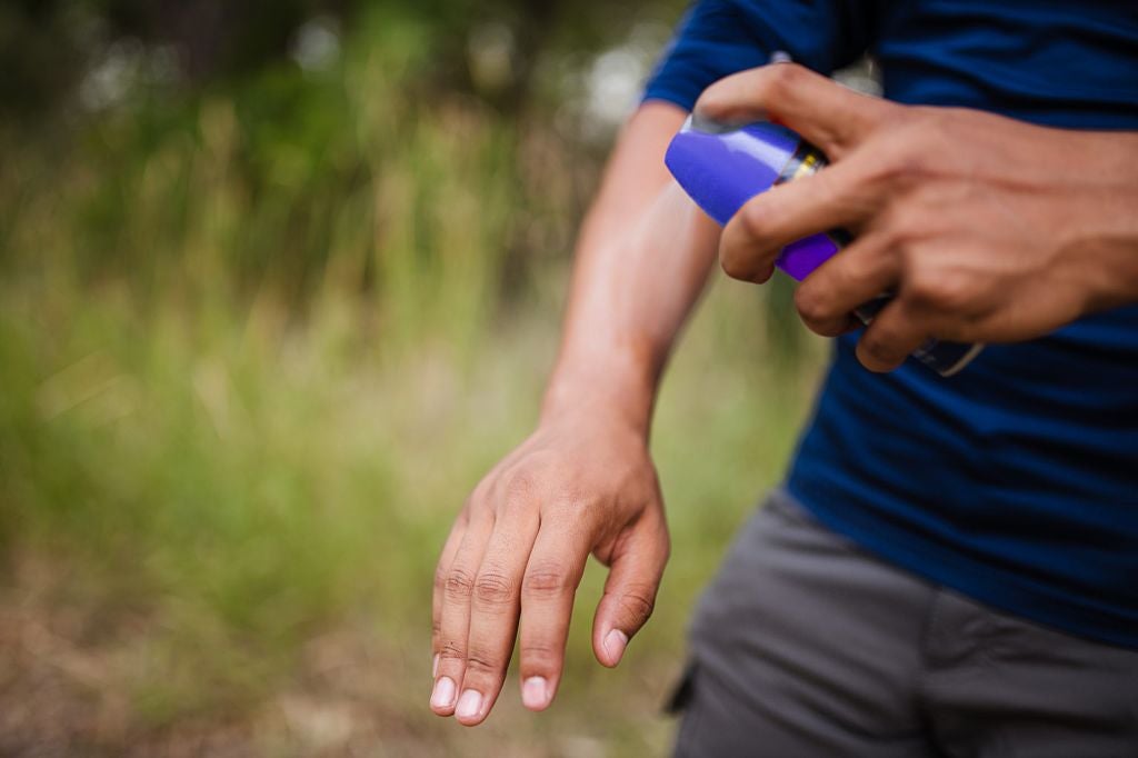 A person sprays insect repellent onto their forearm.
