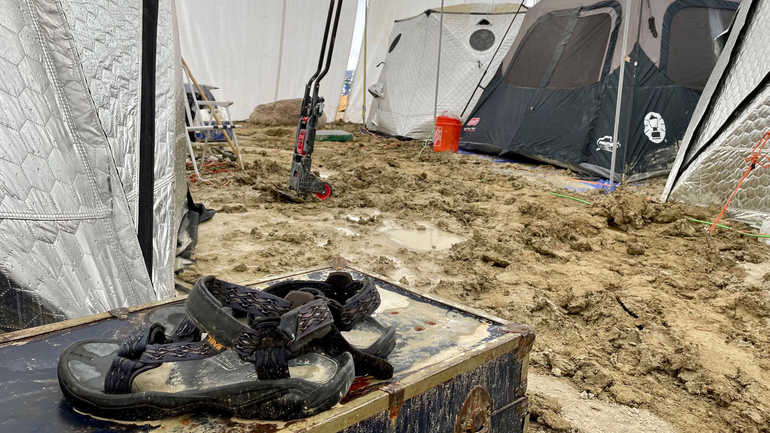 A pair of sandals are seen on a chest in the middle of tents sitting in a muddy desert plain on September 3, 2023. After heavy rains turned the annual Burning Man festival site in Nevada's Black Rock desert into a mud pit, tens of thousands of festivalgoers were stranded.