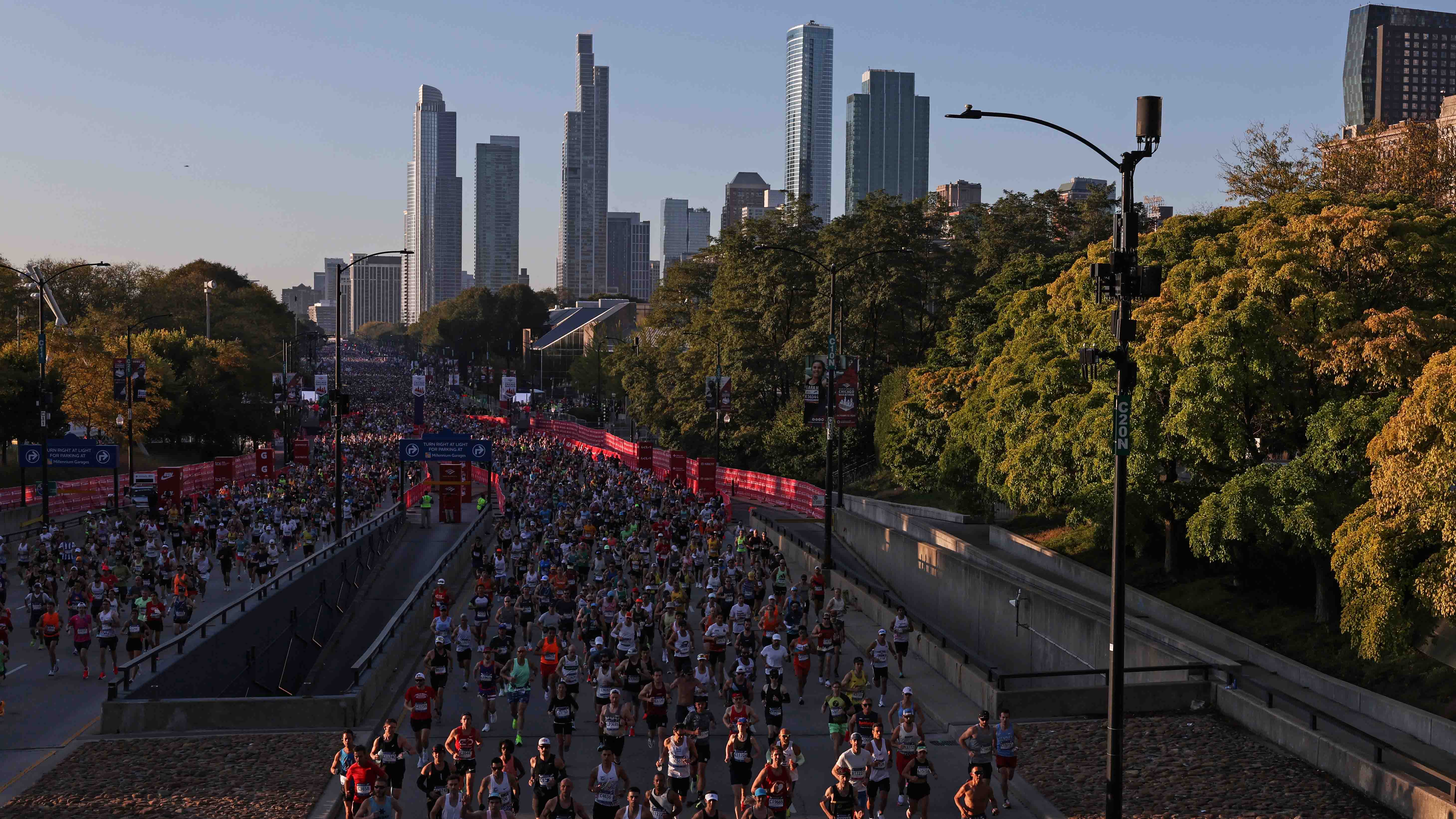 Thousands of marathon runners fill a city street with the Chicago skyline visible in the background