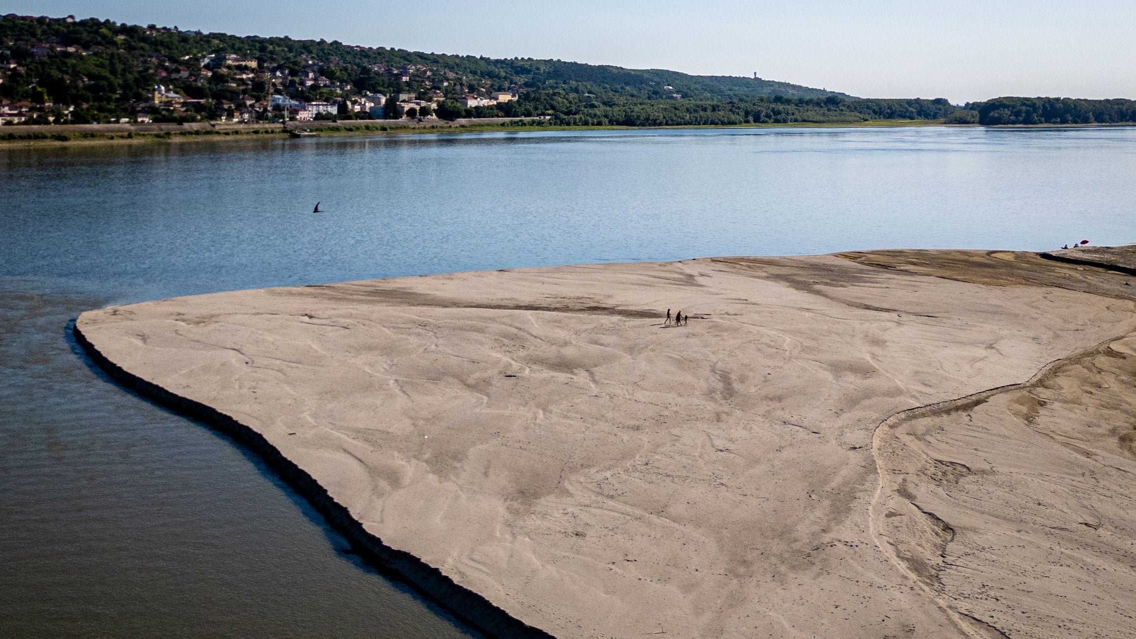 People walk on a bank of sand on the Danube River as usually submerged areas are exposed due to extremely low levels of the water following an extended period of drought in Oltenita, Romania, Saturday, Aug.1, 2026.