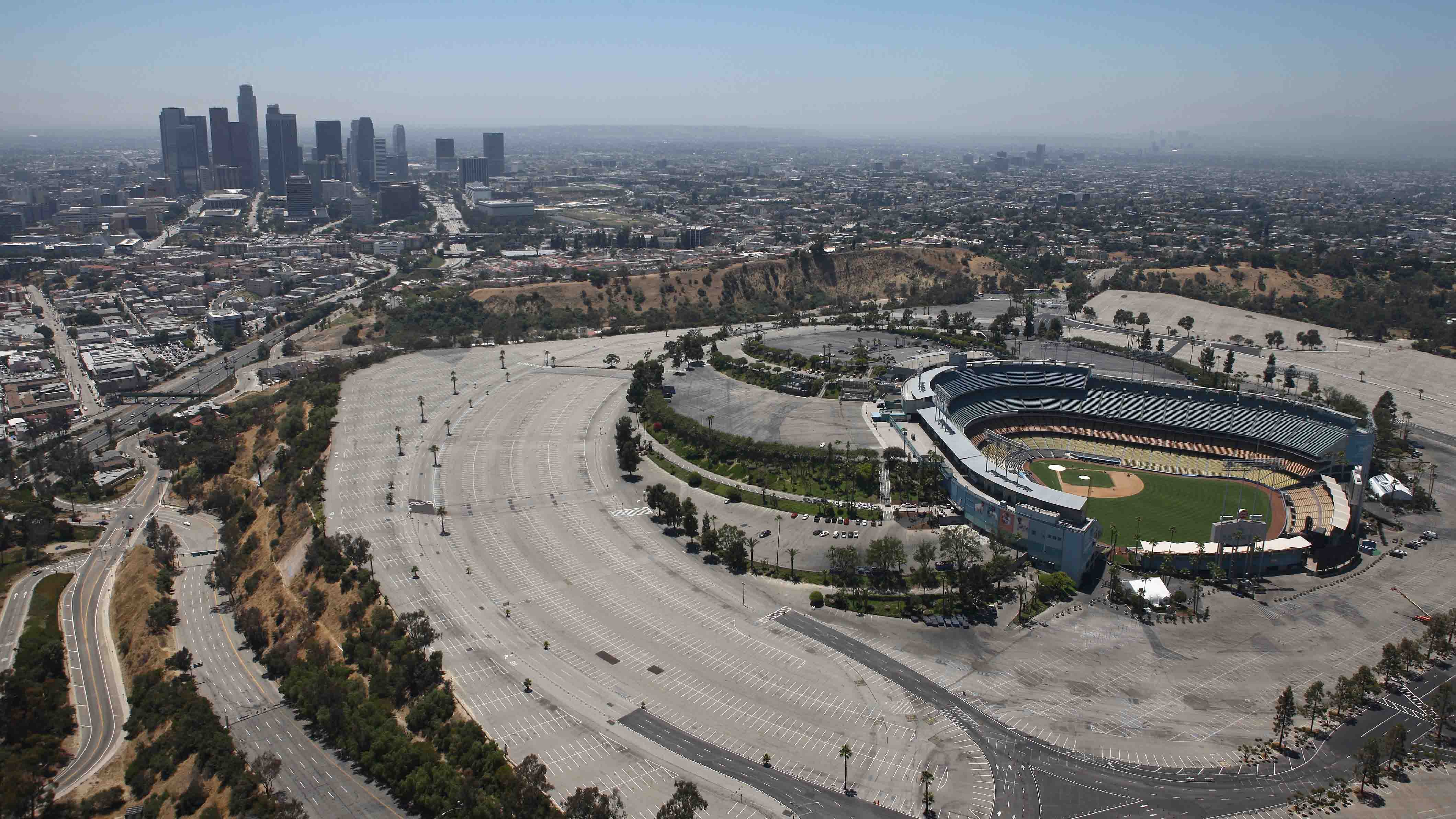 Aerial view of a baseball stadium with empty parking lots and the downtown Los Angeles skyline in the background