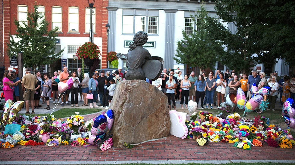 People gather around a statue to place flowers