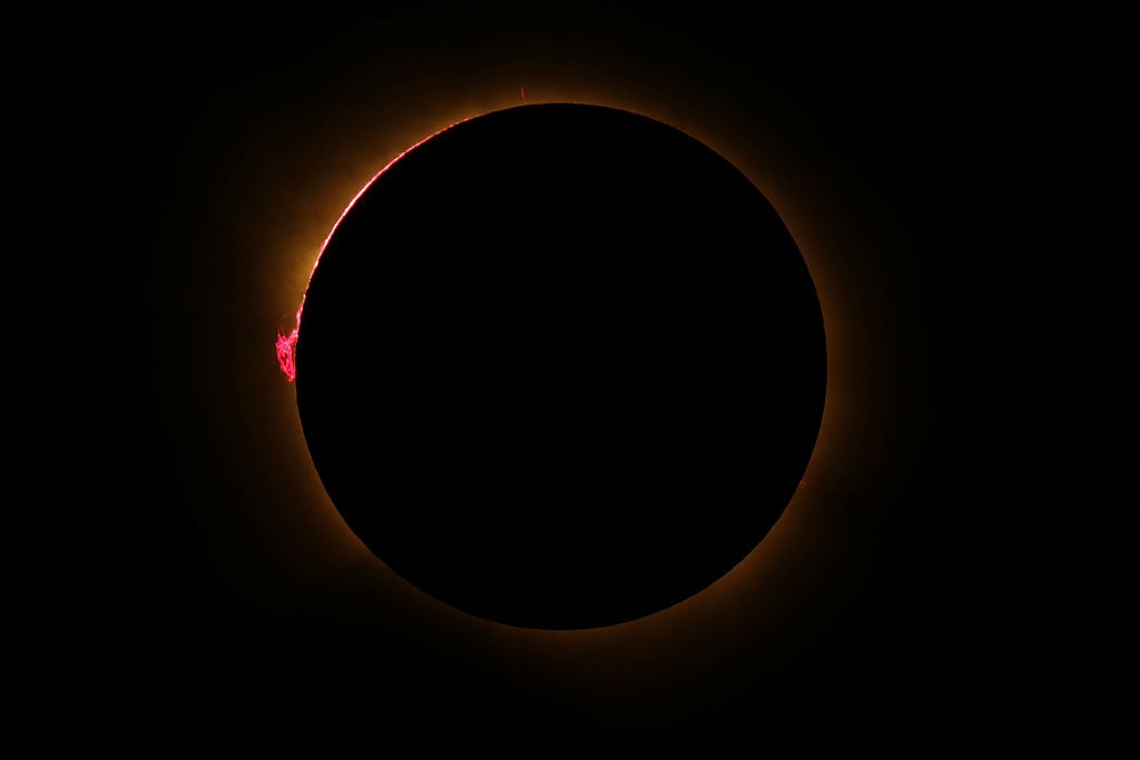 Total solar eclipse showing dark moon silhouette with golden corona and red solar prominence flaring at the edge