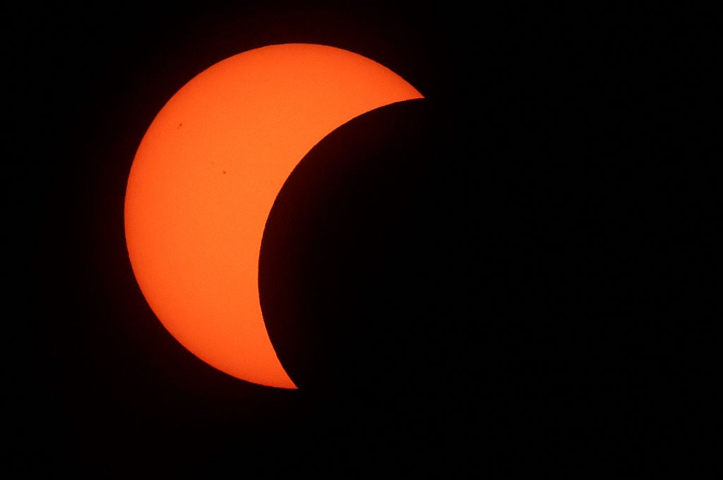 Crescent-shaped orange sun during a partial solar eclipse against a black sky