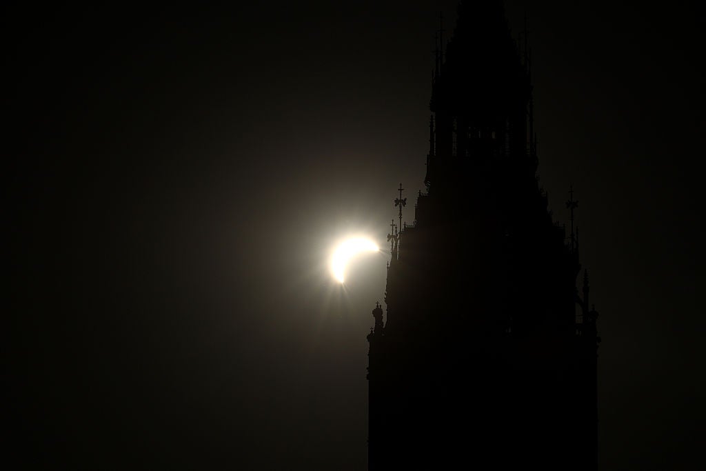 Crescent-shaped partial solar eclipse glowing beside a dark silhouetted Gothic clock tower spire
