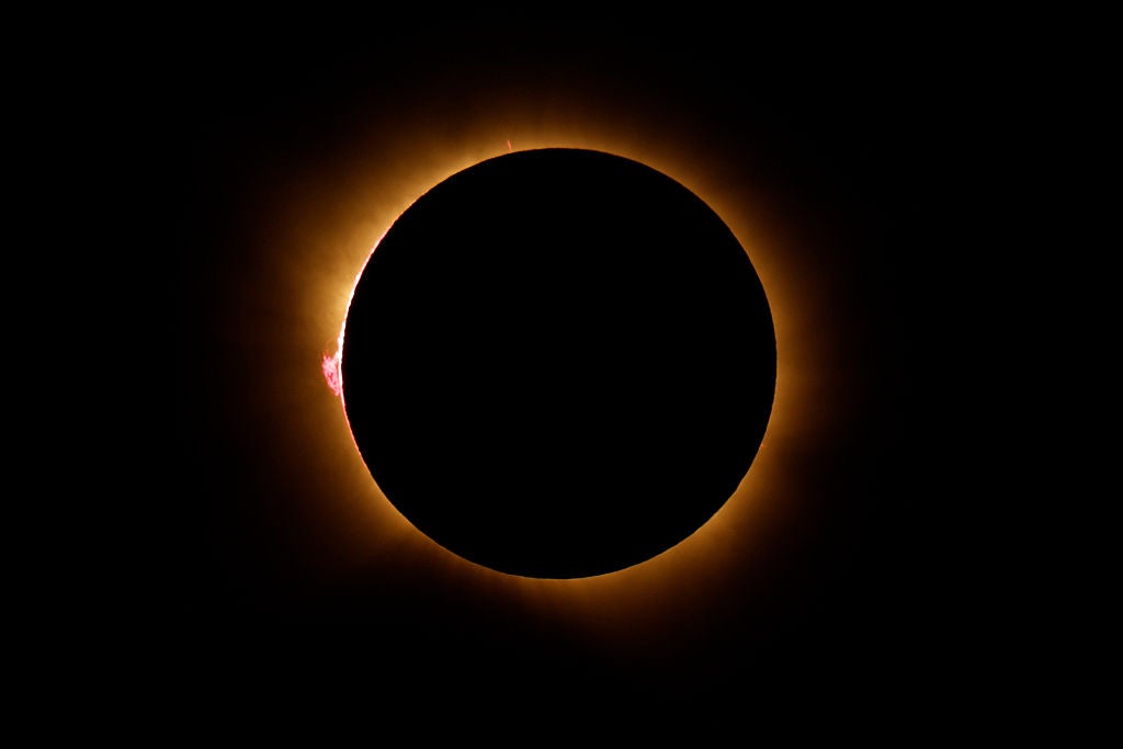 Total solar eclipse showing dark moon silhouette surrounded by glowing golden corona and a red solar prominence