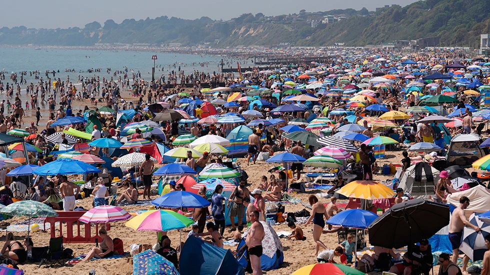 A beach in England is crowded with brightly colored umbrellas.