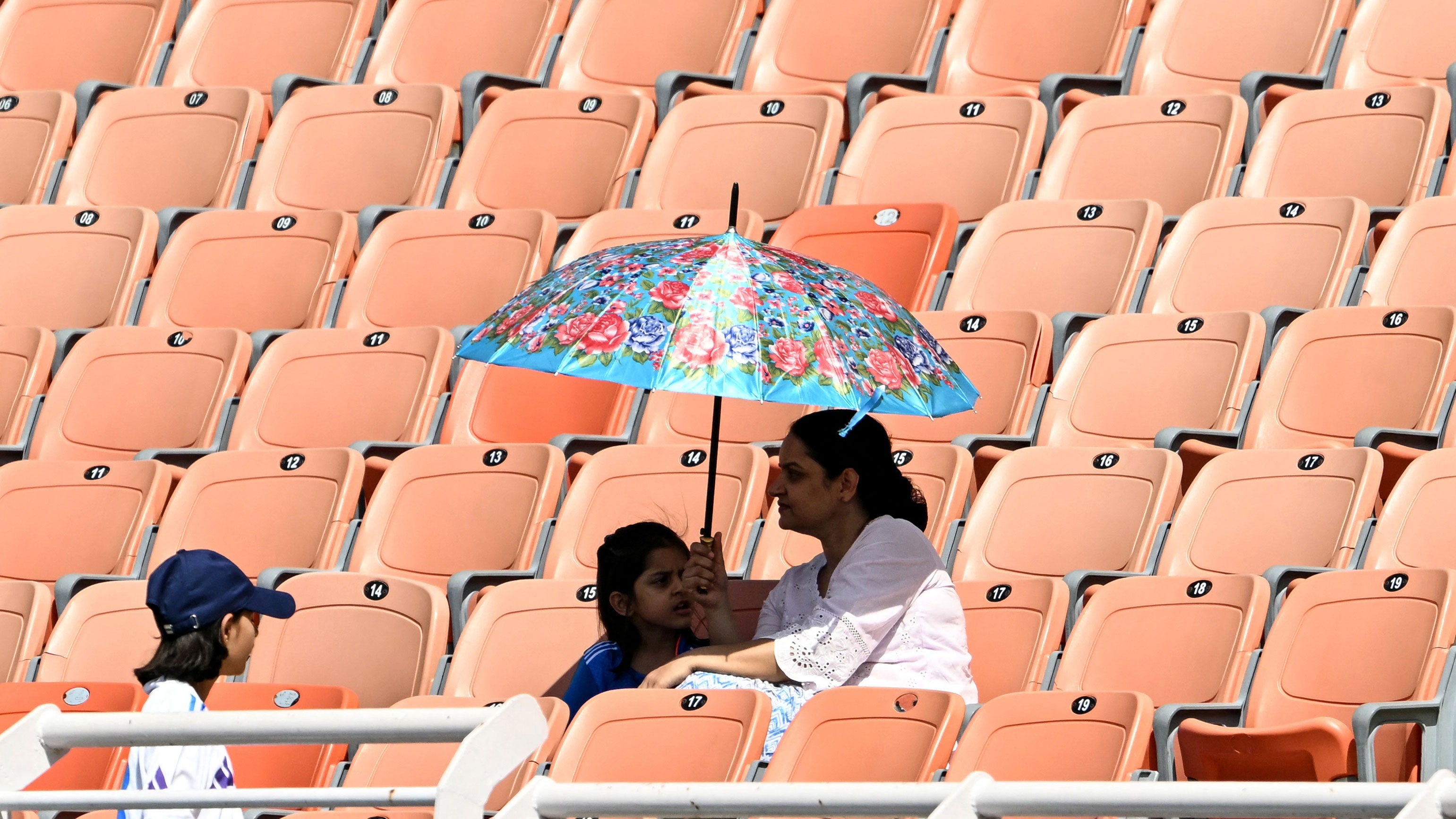 Spectators take shade under umbrellas during the first day of the only Test cricket match between India and Afghanistan at the Maharaja Yadavindra Singh International Cricket Stadium on the outskirts of Chandigarh on June 6, 2026. 