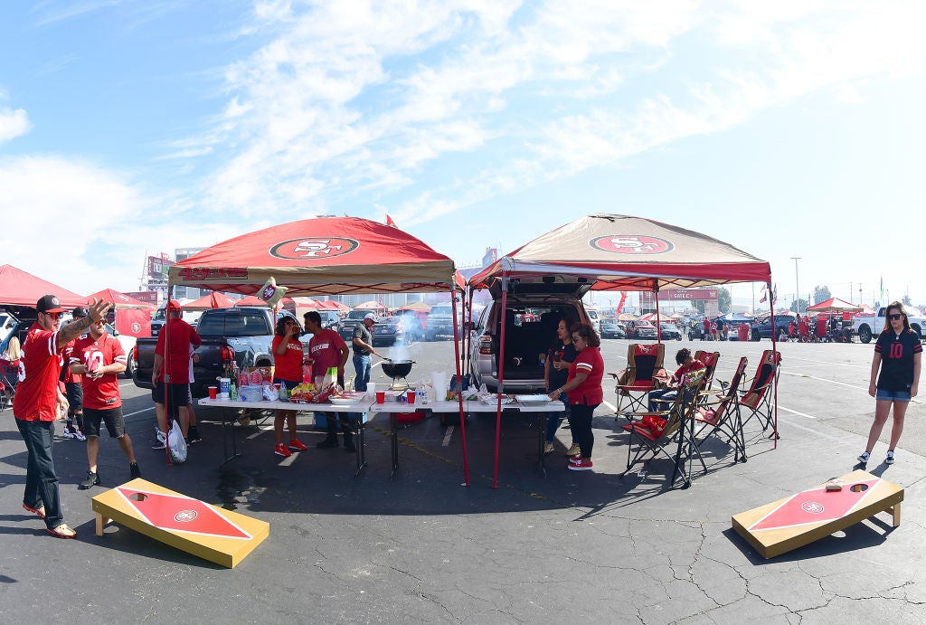 Football fans tailgating, grilling, and playing cornhole.
