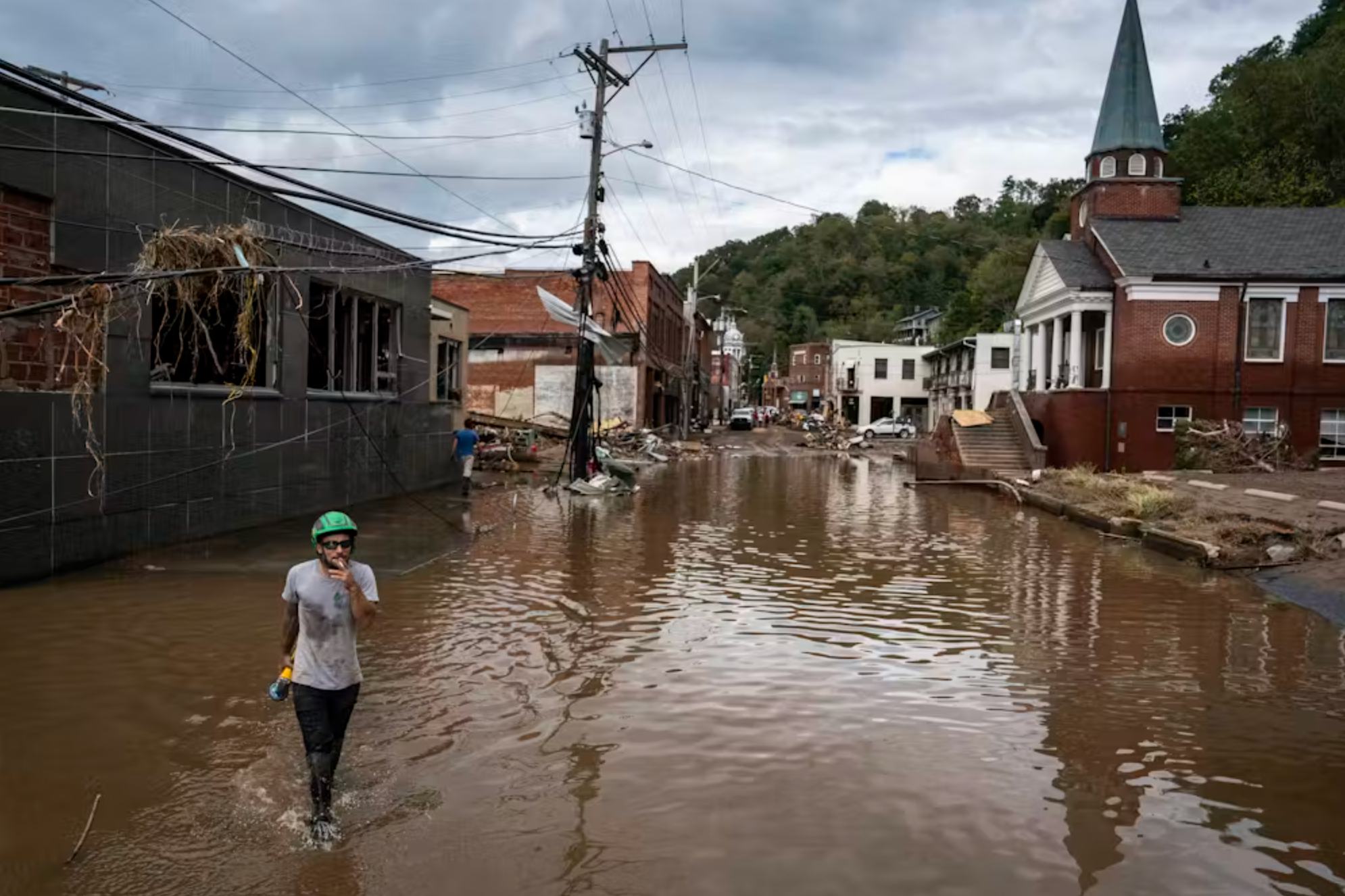 A person walks through floodwaters with a church in the background