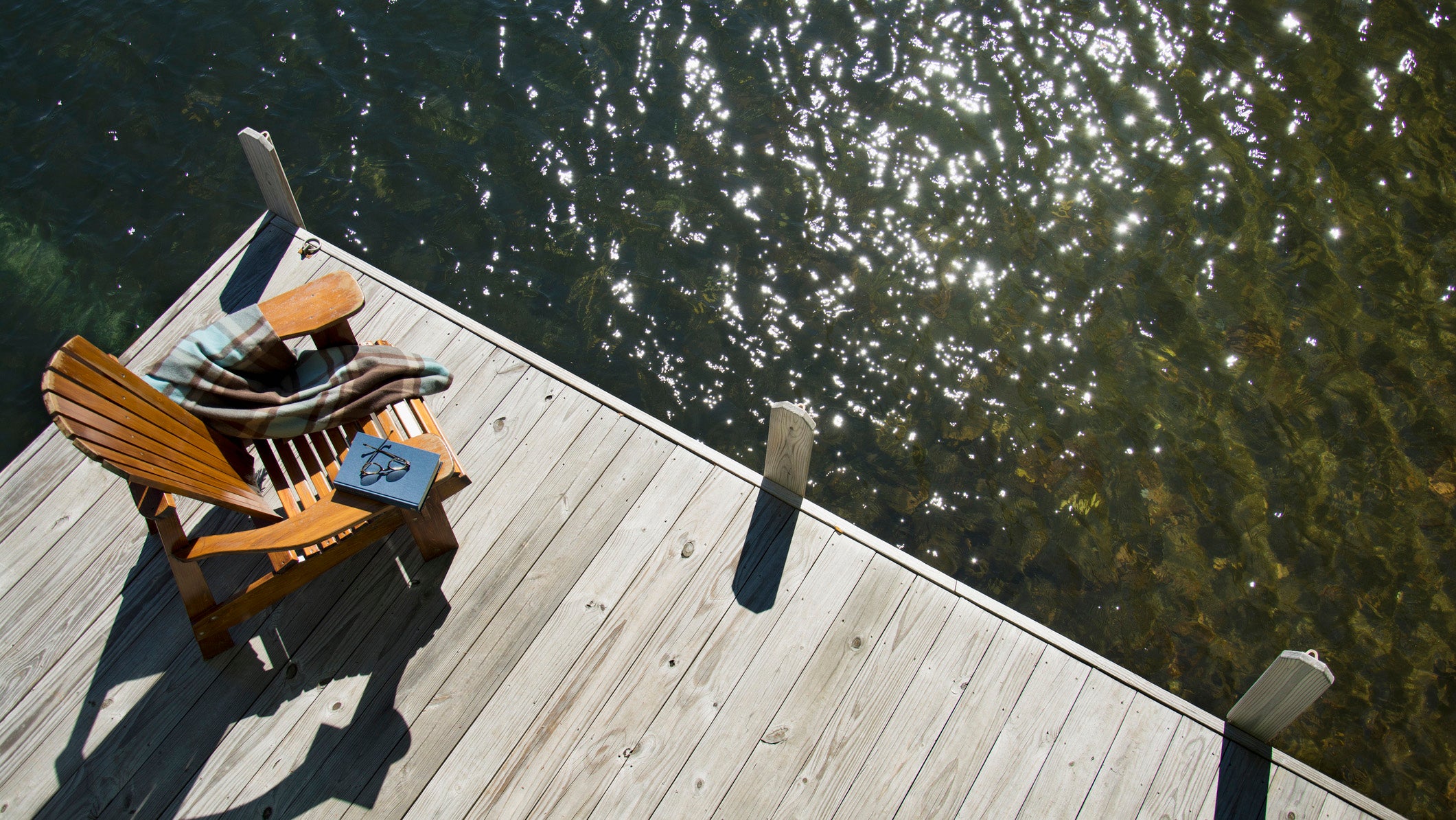 Overhead view of Adirondack chair book and blanket on wooden pier in Lake Placid, New York.