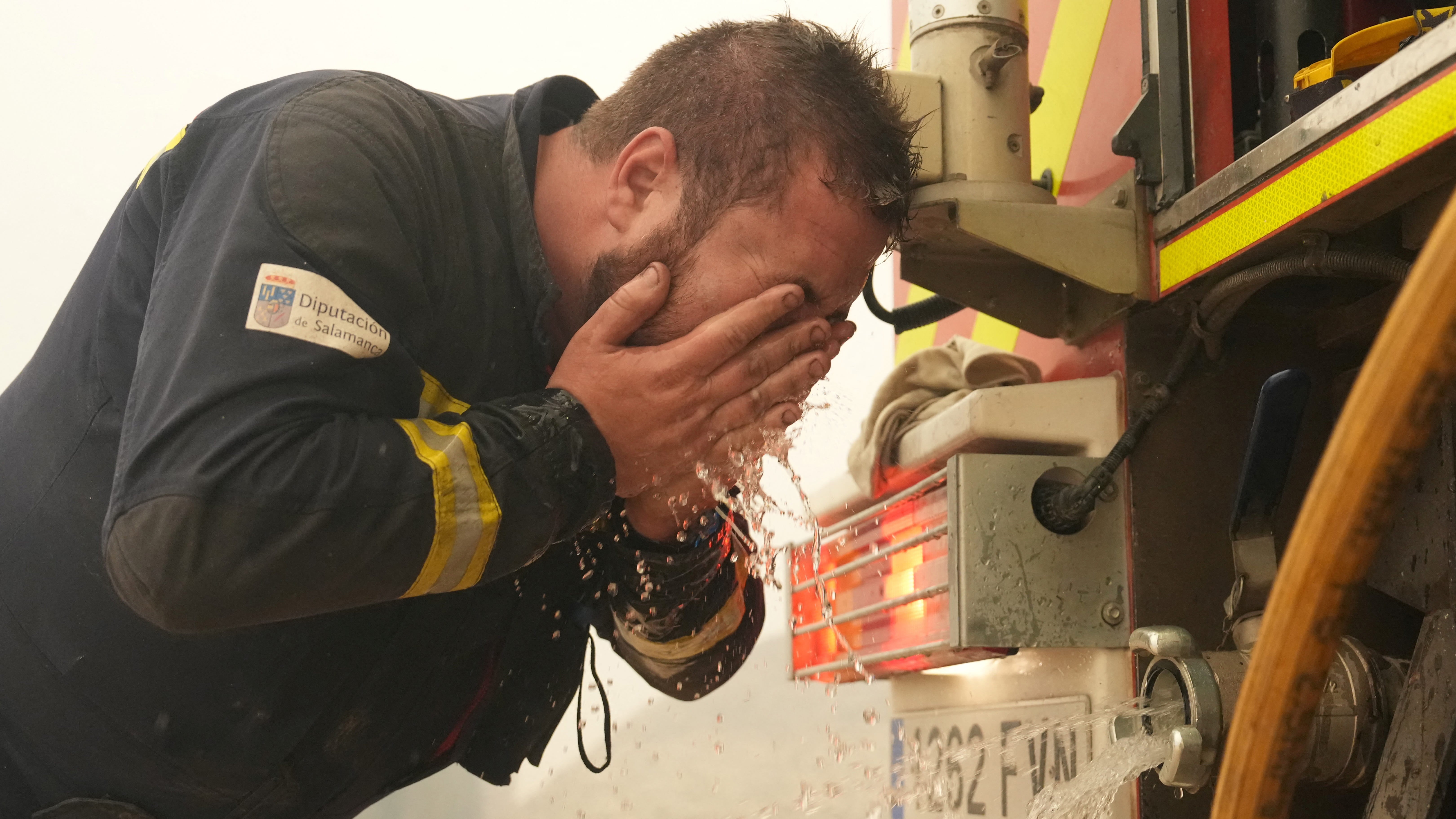 Firefighter in uniform rinsing his face with water beside a fire truck pump panel
