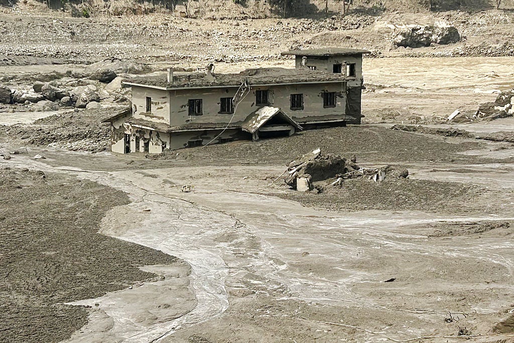 Two-story building partially buried in thick mud and debris after a flood or landslide