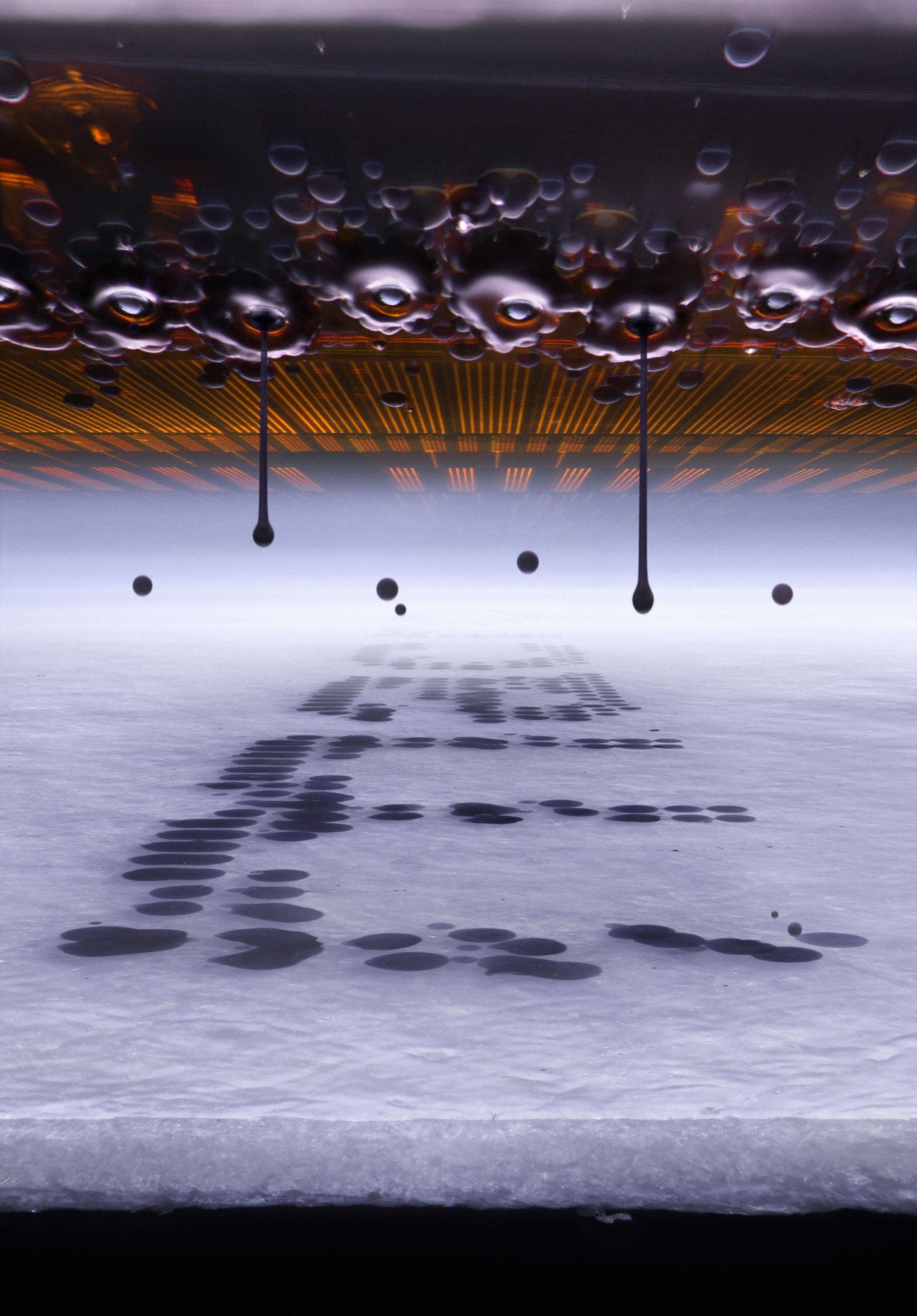 Dark liquid droplets falling from a glowing orange ceiling onto a pale surface, forming splattered patterns below