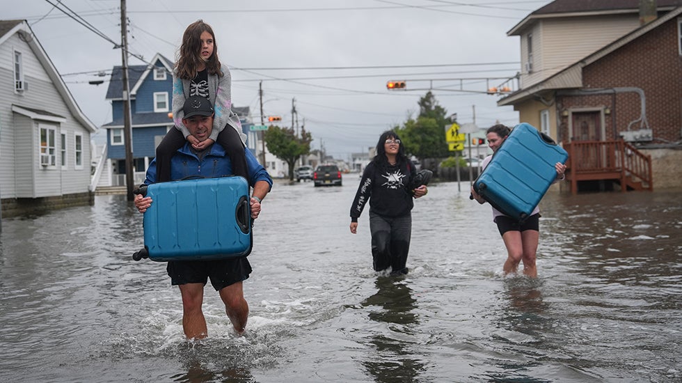 A family of four walk on a flooded street while carrying suitcases