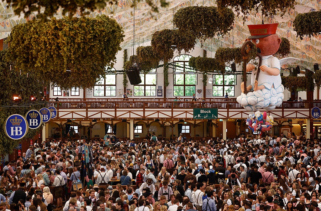 Wide interior view of a crowded, decorated beer tent at Munich's Oktoberfest with long communal tables.