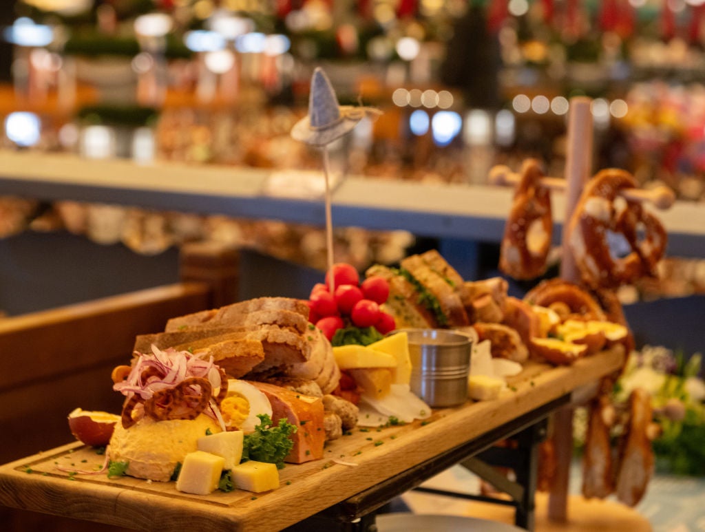 Close-up of a wooden platter loaded with pretzels, sausages and cheese on a table at an Oktoberfest beer tent.