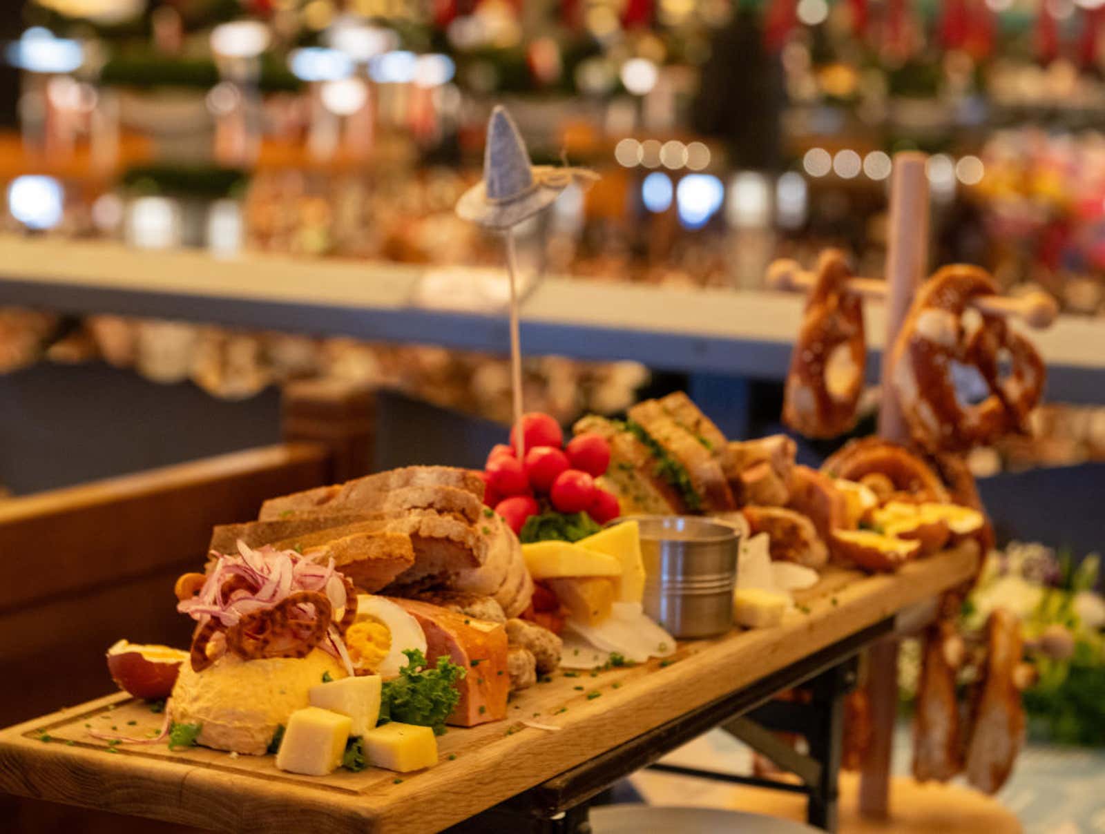 Close-up of a wooden platter loaded with pretzels, sausages and cheese on a table at an Oktoberfest beer tent.