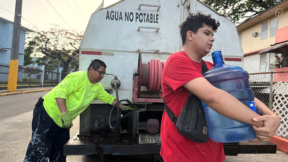 FILE - Bryan Pérez hauls a five-gallon water jug to his apartment in the Villa Kennedy public housing complex in San Juan
