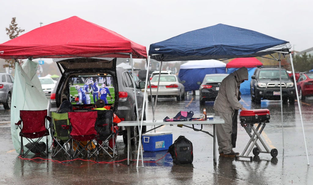 Heavy rain falls as a tailgater grills outside. 