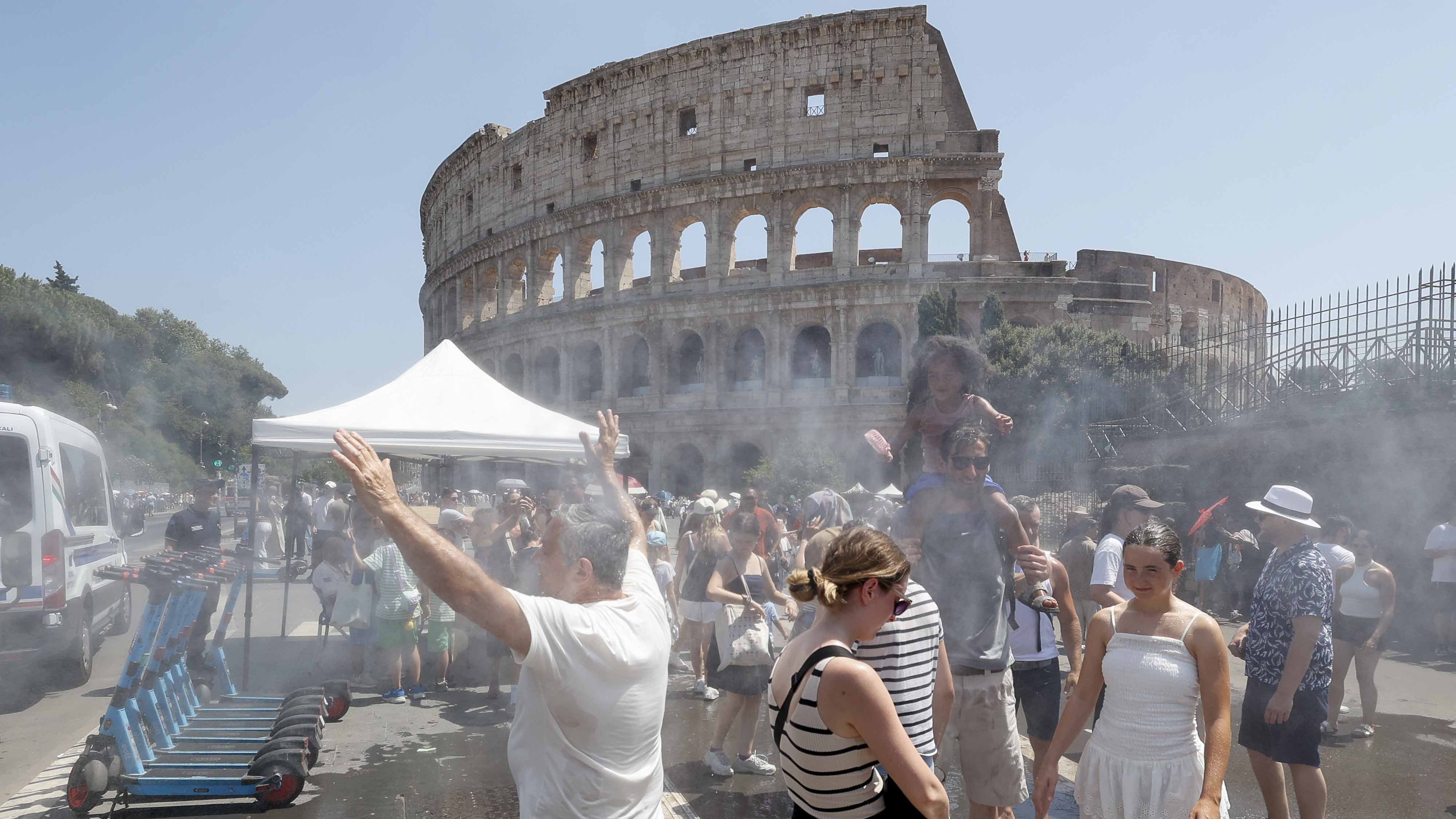 Tourists cool off under misting sprays near the Colosseum in Rome during hot weather.