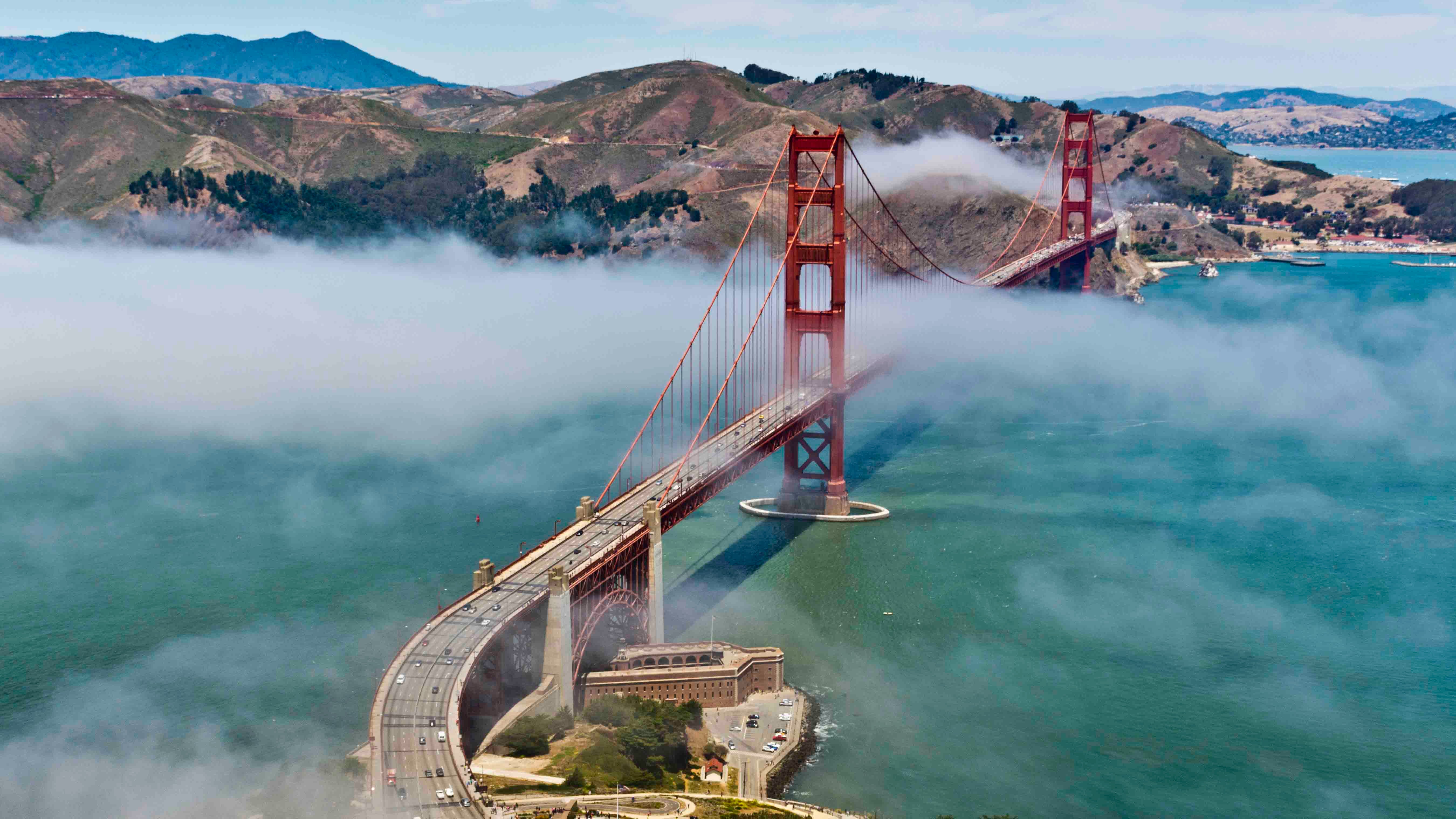 Aerial view of the Golden Gate Bridge shrouded in fog with hills and bay waters in the background