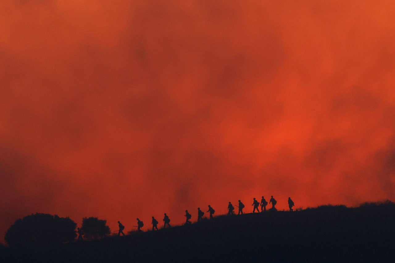 Firefighters are silhouetted walking amid the firing operation to control the Sandy Fire, Tuesday, May 19, 2026, in Simi Valley, California.