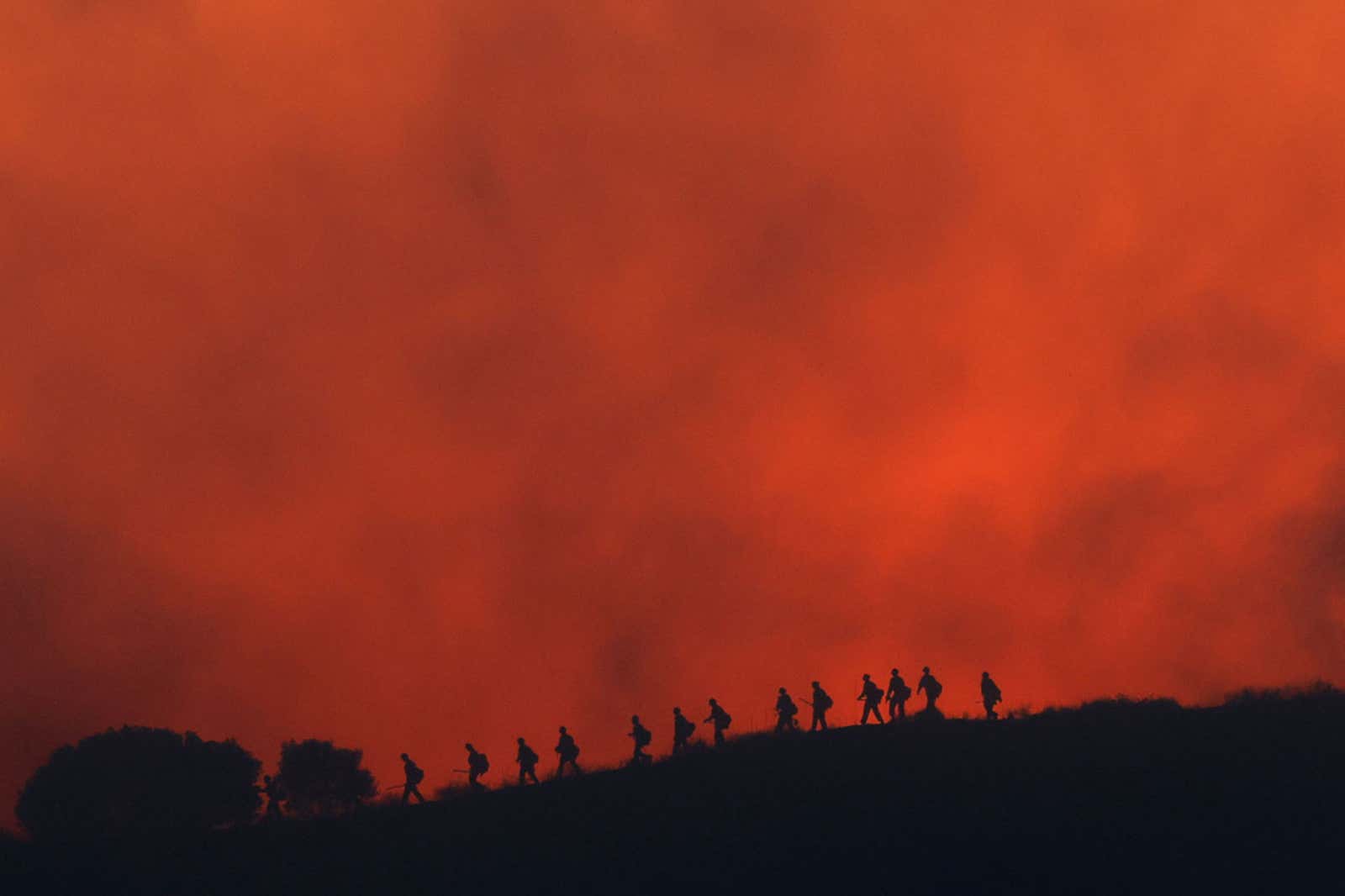 Firefighters are silhouetted walking amid the firing operation to control the Sandy Fire, Tuesday, May 19, 2026, in Simi Valley, California.