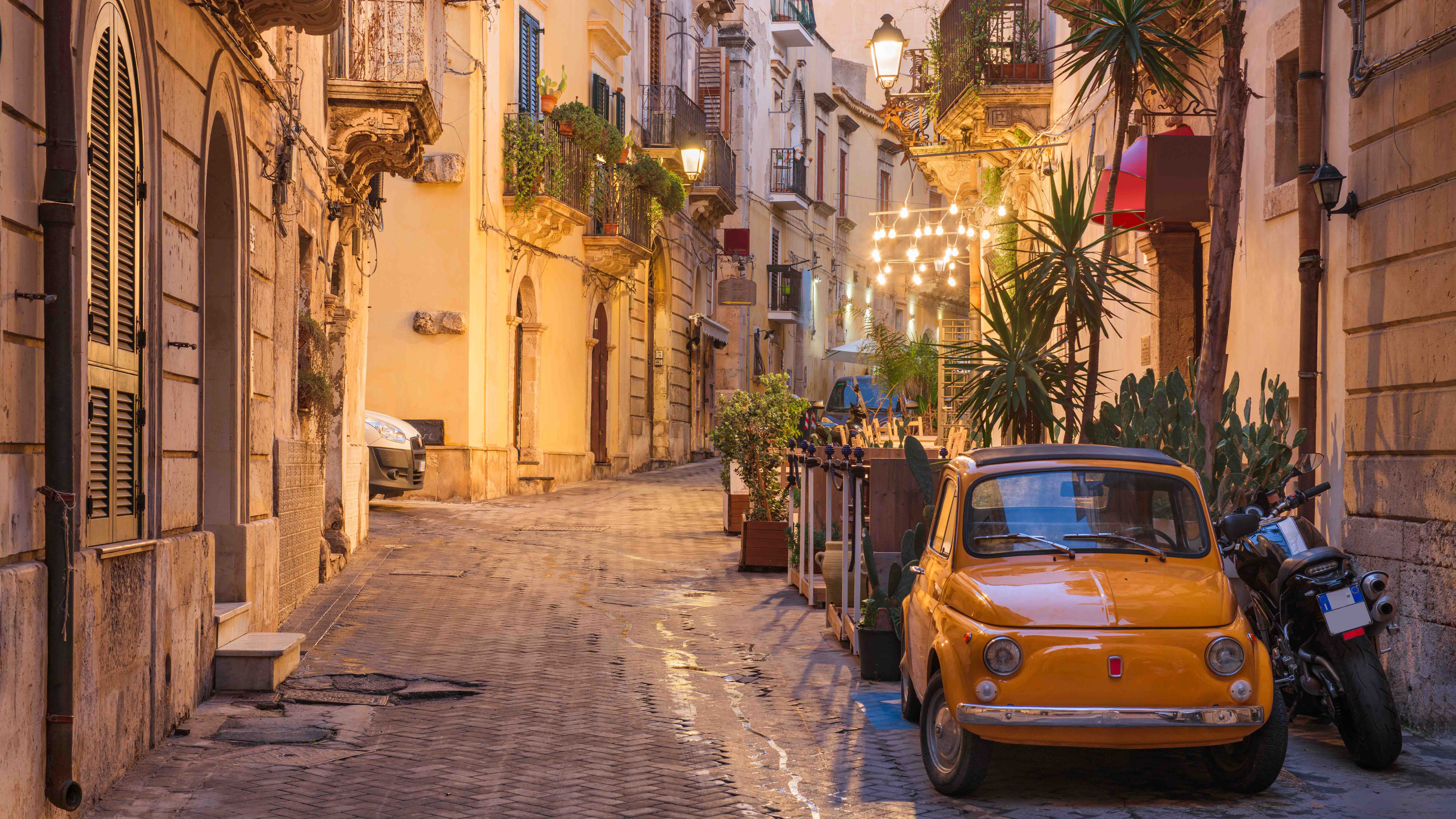 Vintage orange Fiat 500 parked on a narrow cobblestone street lined with historic buildings and warm streetlights at dusk