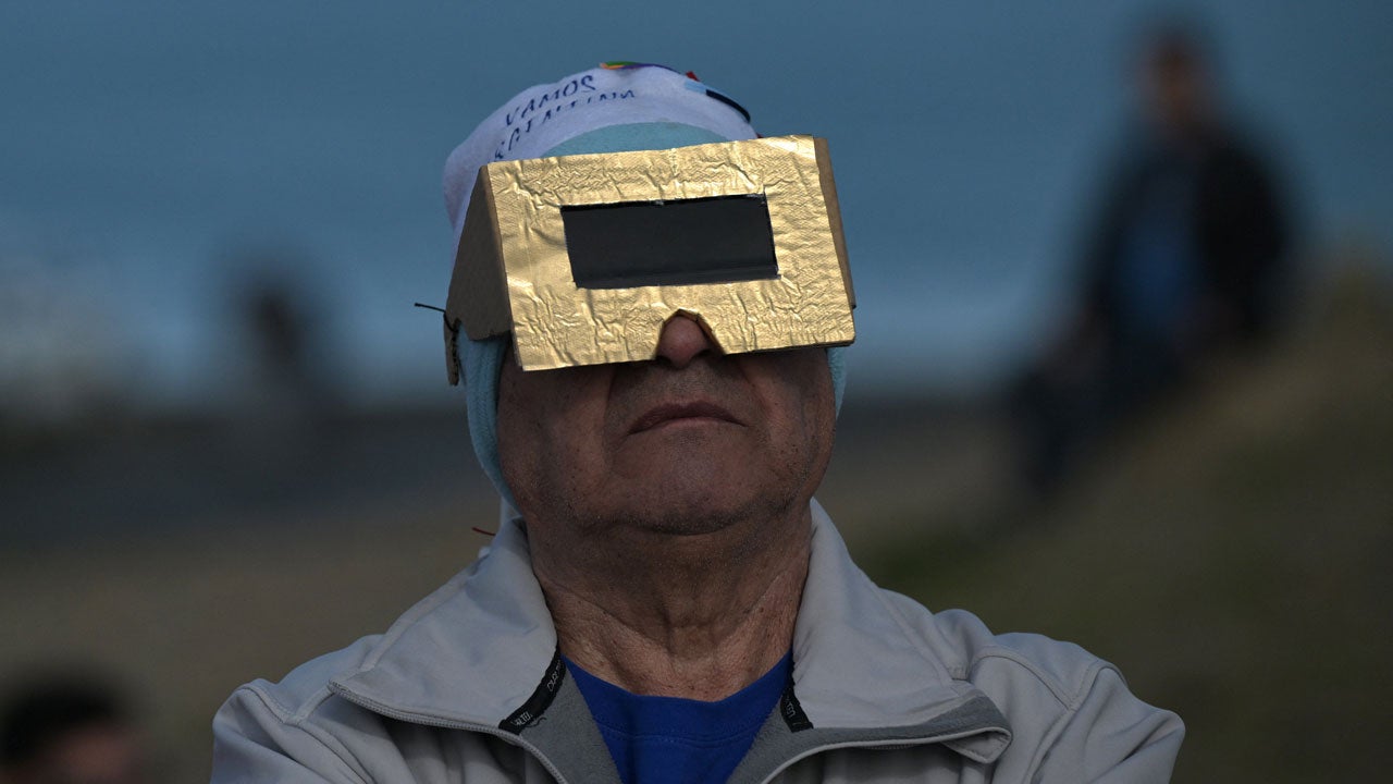 Man wearing gold cardboard eclipse glasses and a knit cap looks upward outdoors