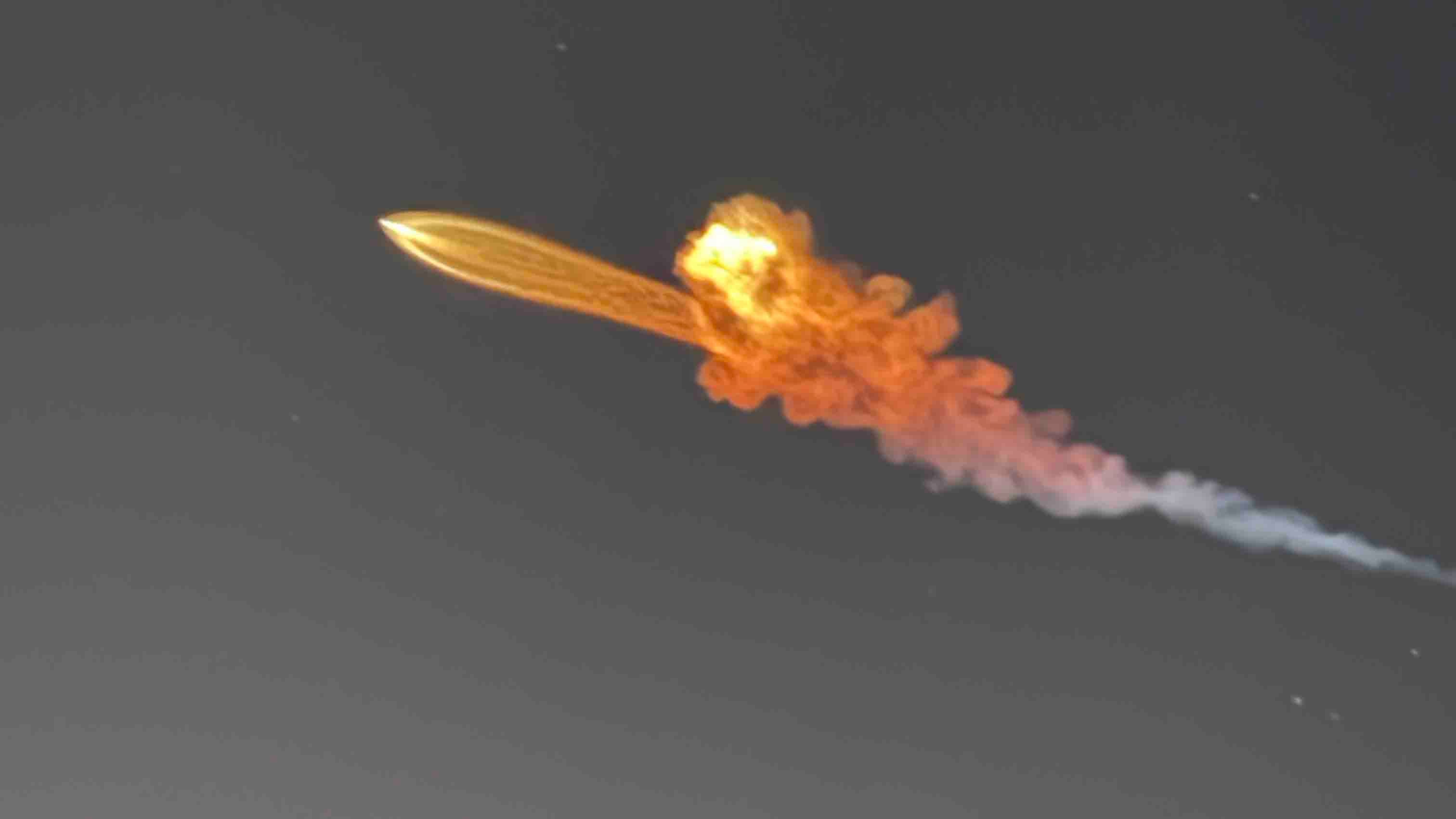 Rocket ascending through night sky with bright fiery explosion and trailing smoke plume