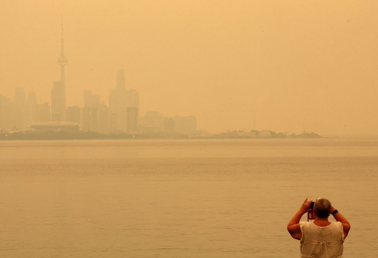 Smoky skyline across water with a man photographing from the shore