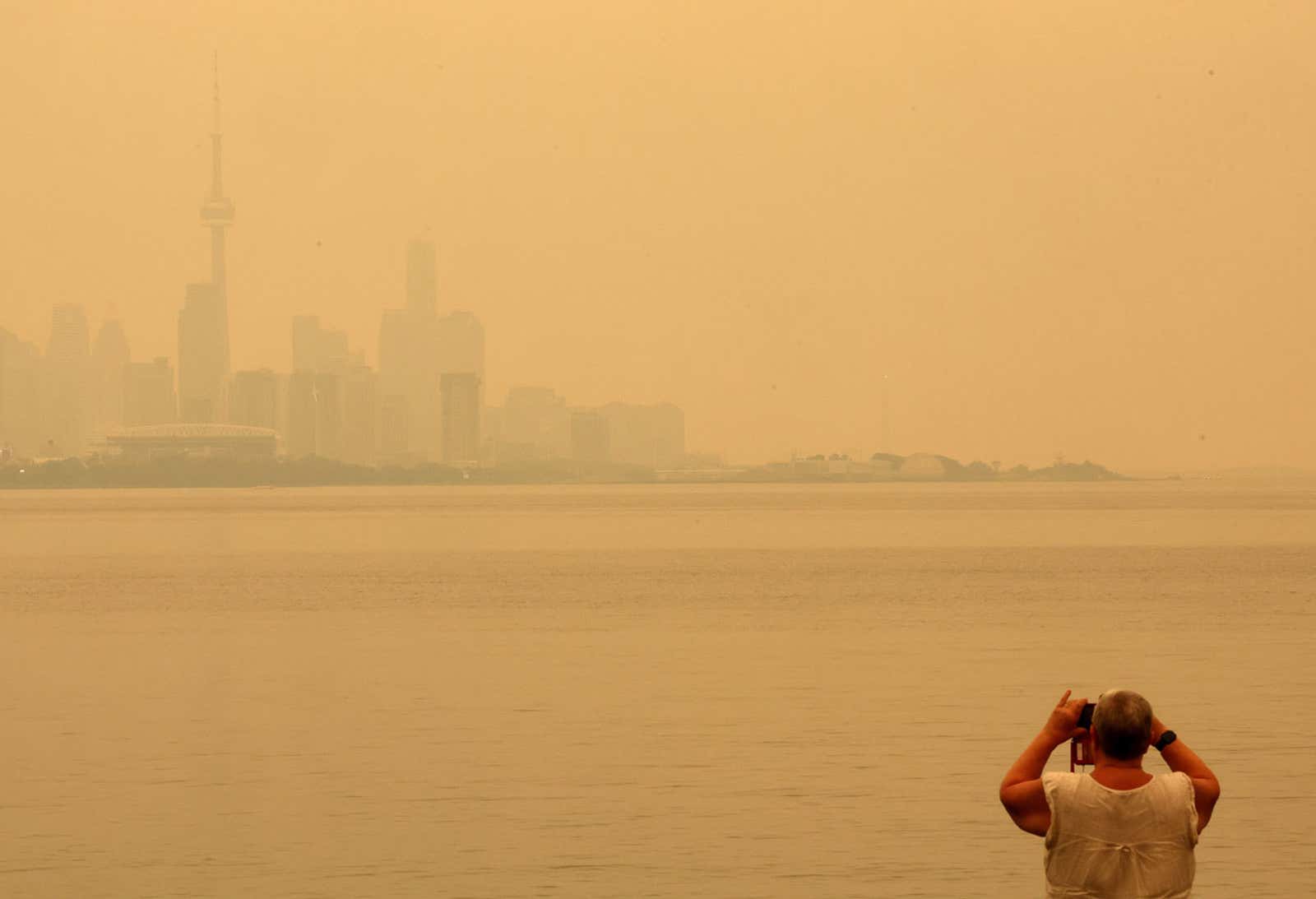 Smoky skyline across water with a man photographing from the shore