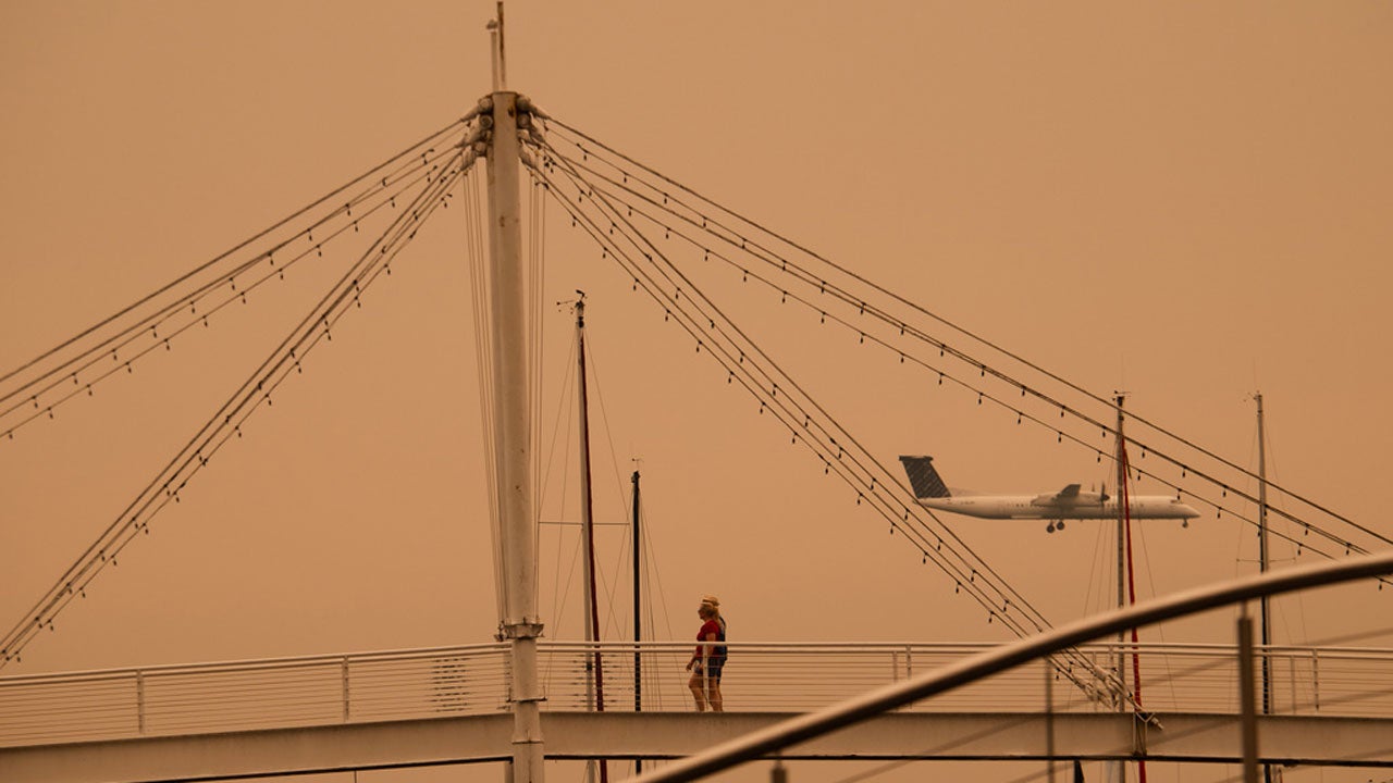 Suspension bridge with a person walking and an airplane approaching in an orange sky