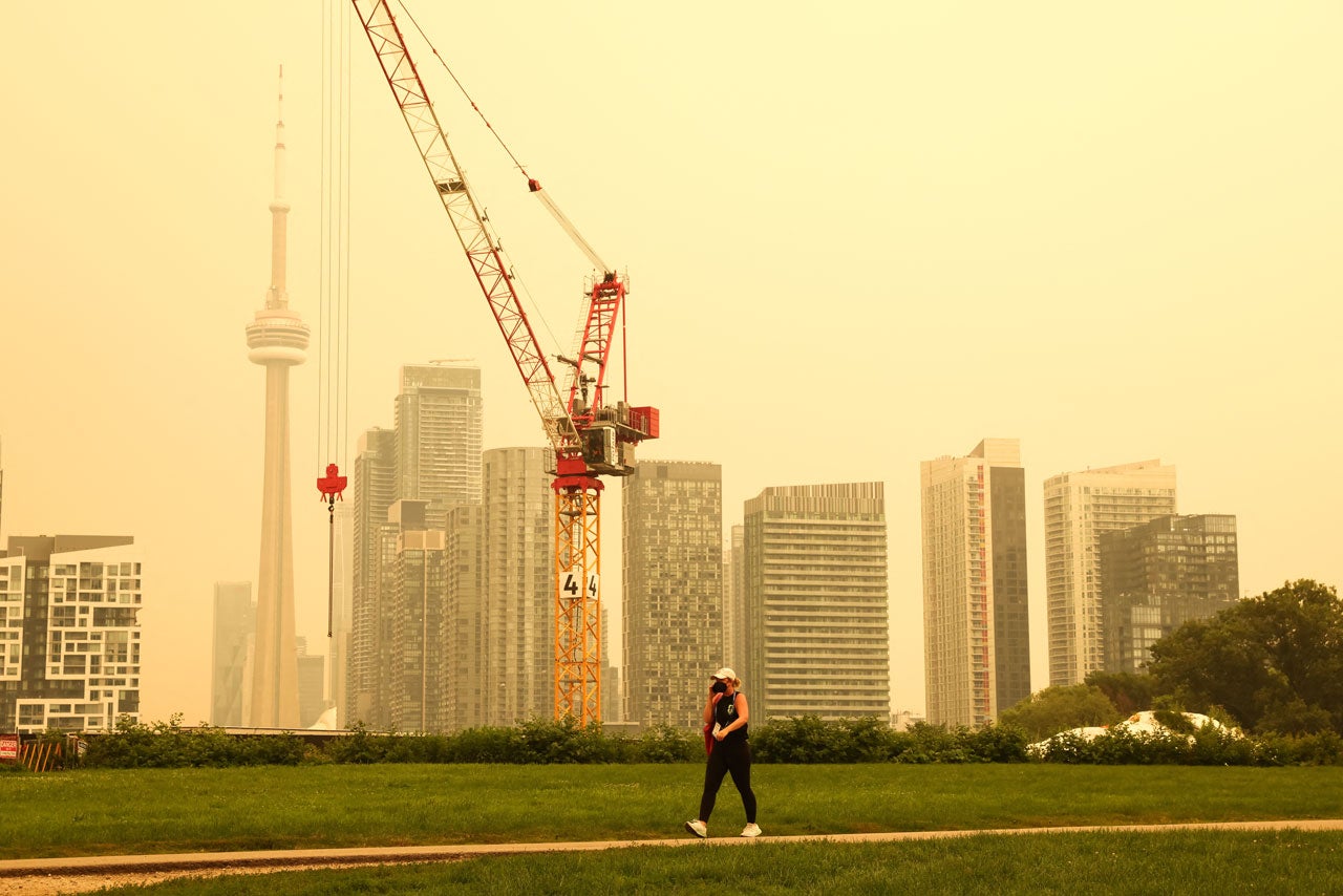 City skyline under hazy yellow sky with a crane and a walking person in the foreground