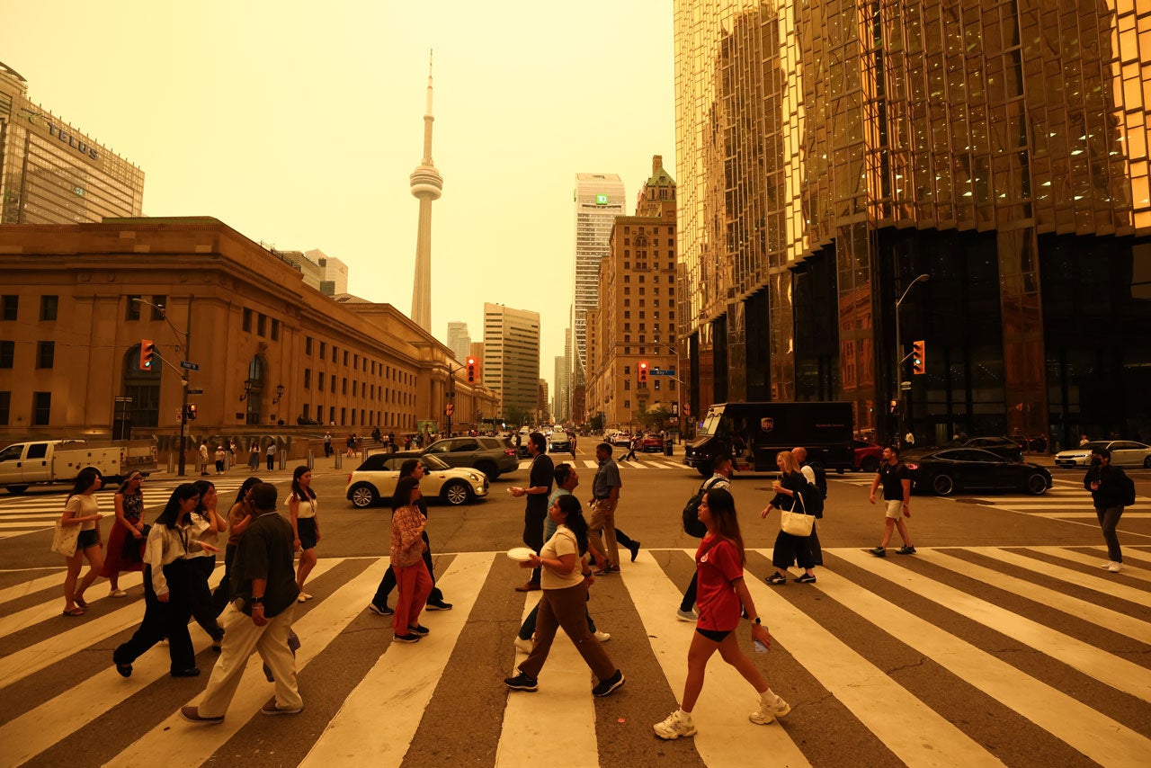 Pedestrians crossing a city street with the CN Tower and skyscrapers in the background