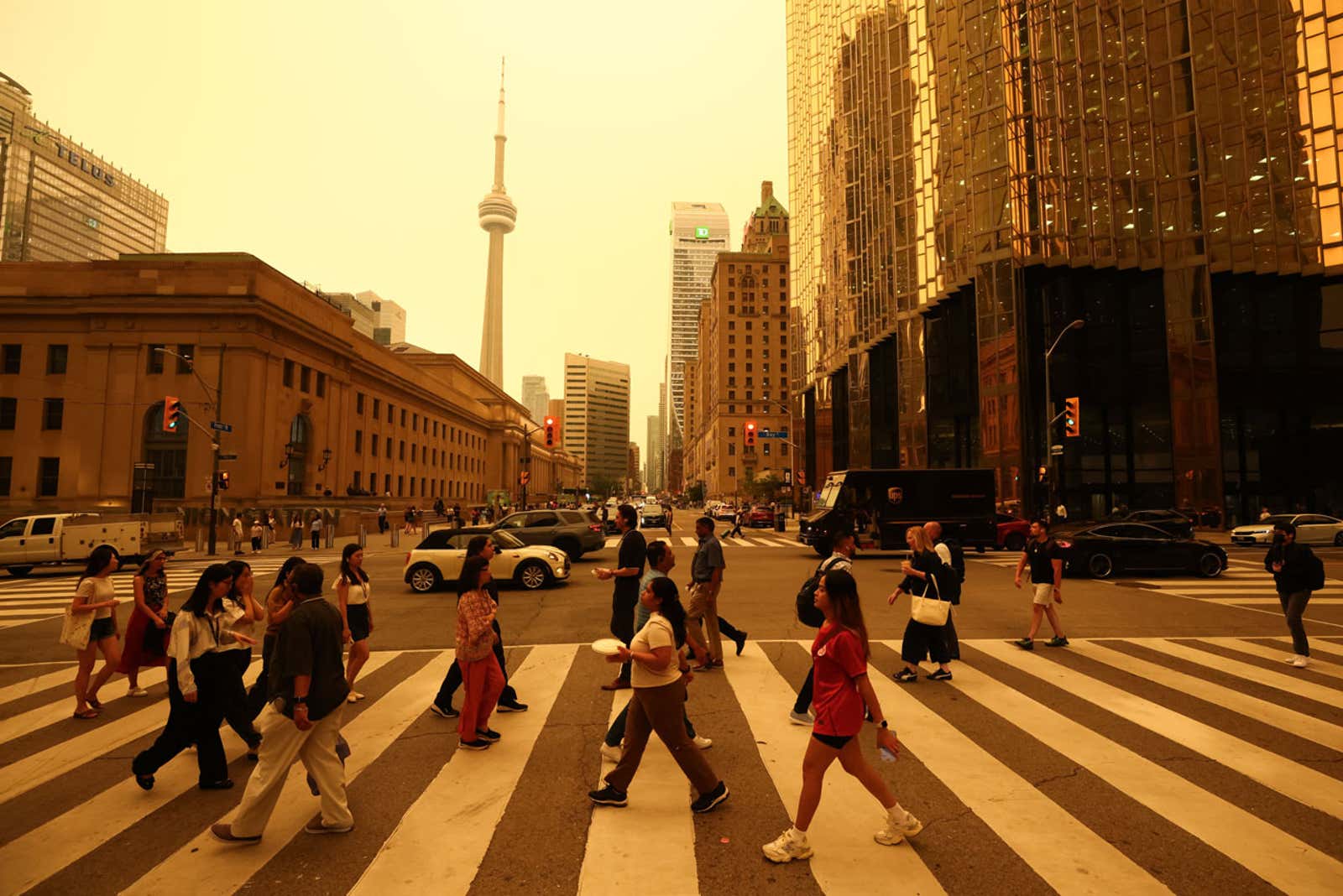 Pedestrians crossing a city street with the CN Tower and skyscrapers in the background