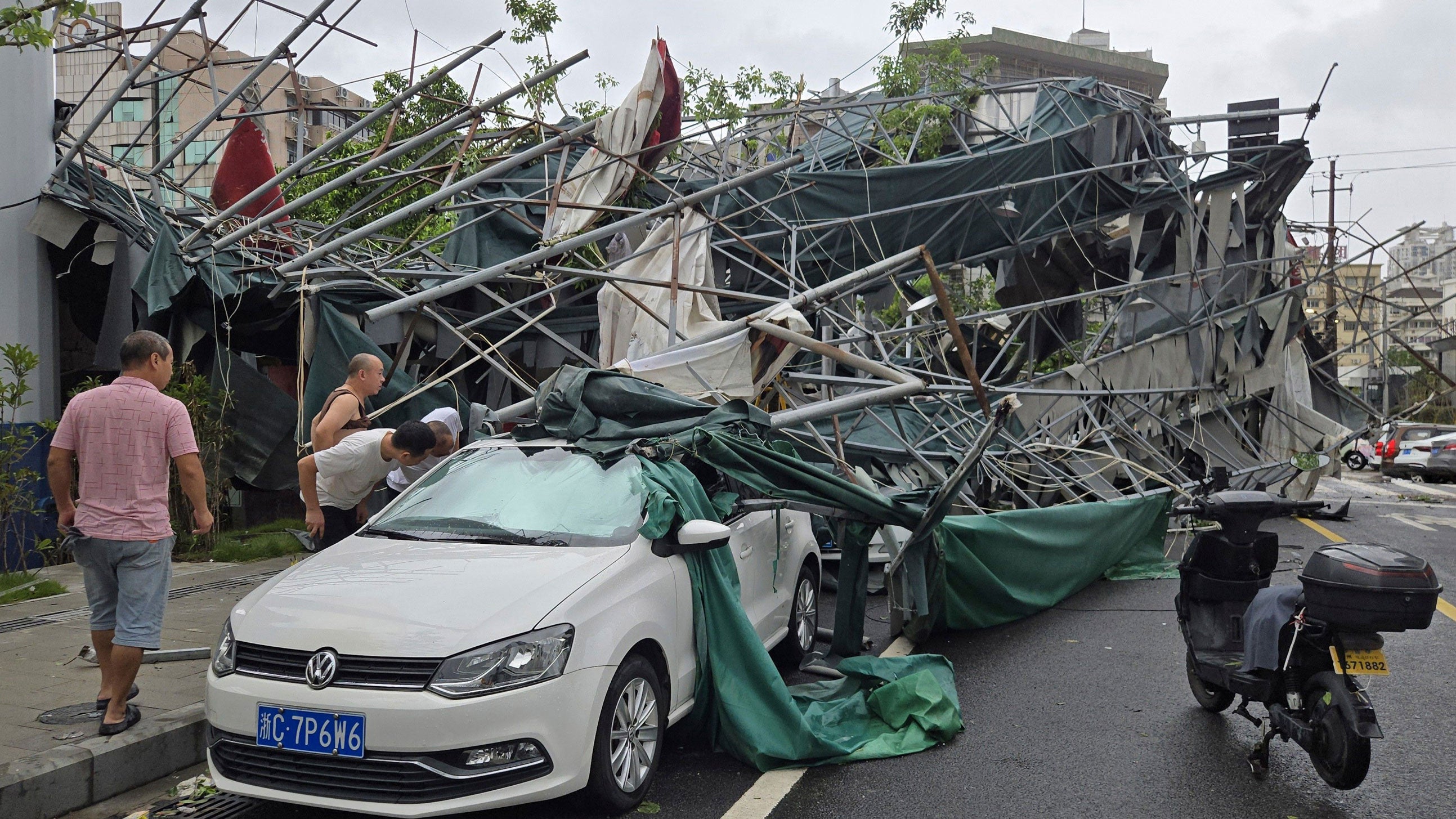 People look inside a car pinned by a fallen scaffolding structure after Typhoon Dolphin hit the area in Wenzhou, eastern China's Zhejiang province, Monday, Aug. 10, 2026.