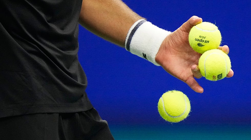 A hand holding two tennis balls drops a third ball
