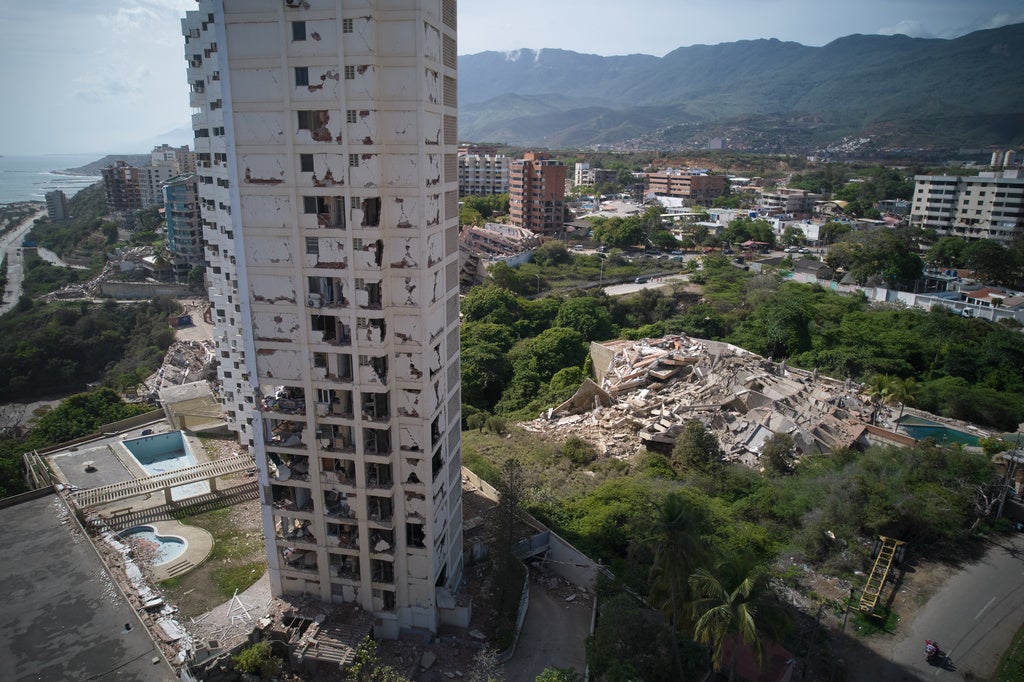 Aerial view of earthquake-damaged high-rise building with collapsed structure amid coastal city with mountains in background