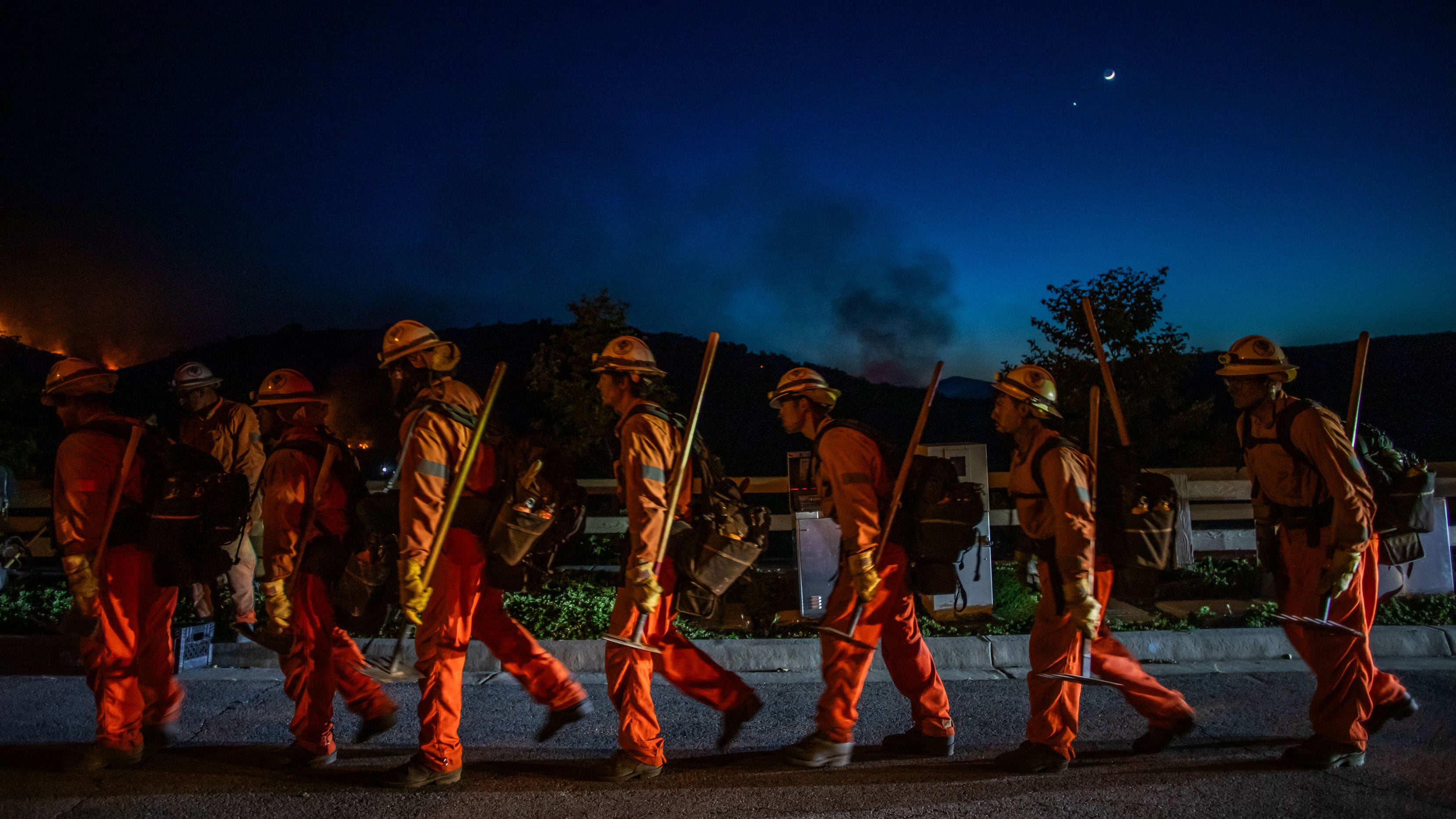 Inmate firefighters walk back to their fire truck after combating the Sandy Fire in Simi Valley, California on May 18, 2026. A brush fire broke out on May 18 in the suburbs of Los Angeles, spreading rapidly and prompting authorities to issue evacuation orders for thousands of residents. Dubbed the Sandy Fire, the blaze broke out late morning in Simi Valley, a city of roughly 125,000 residents about 40 miles northwest of downtown Los Angeles.