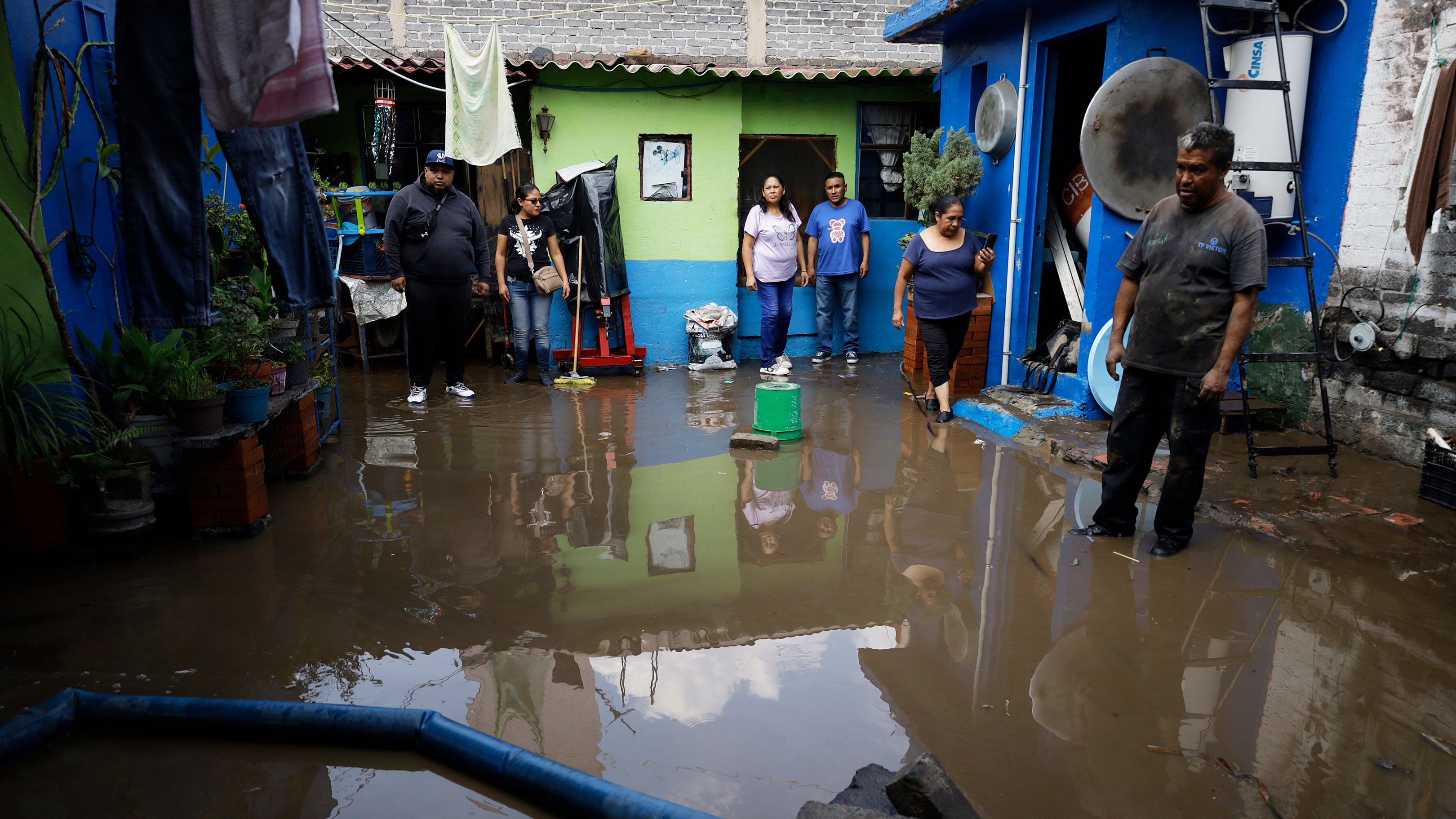 People bail water from their homes in the Iztapalapa borough of Mexico City, Mexico, on May 13, 2026, after a major water leak causes a sinkhole that floods houses and streets in the area. A large emergency operation involving civil protection, firefighters, and police is deployed to address the situation.