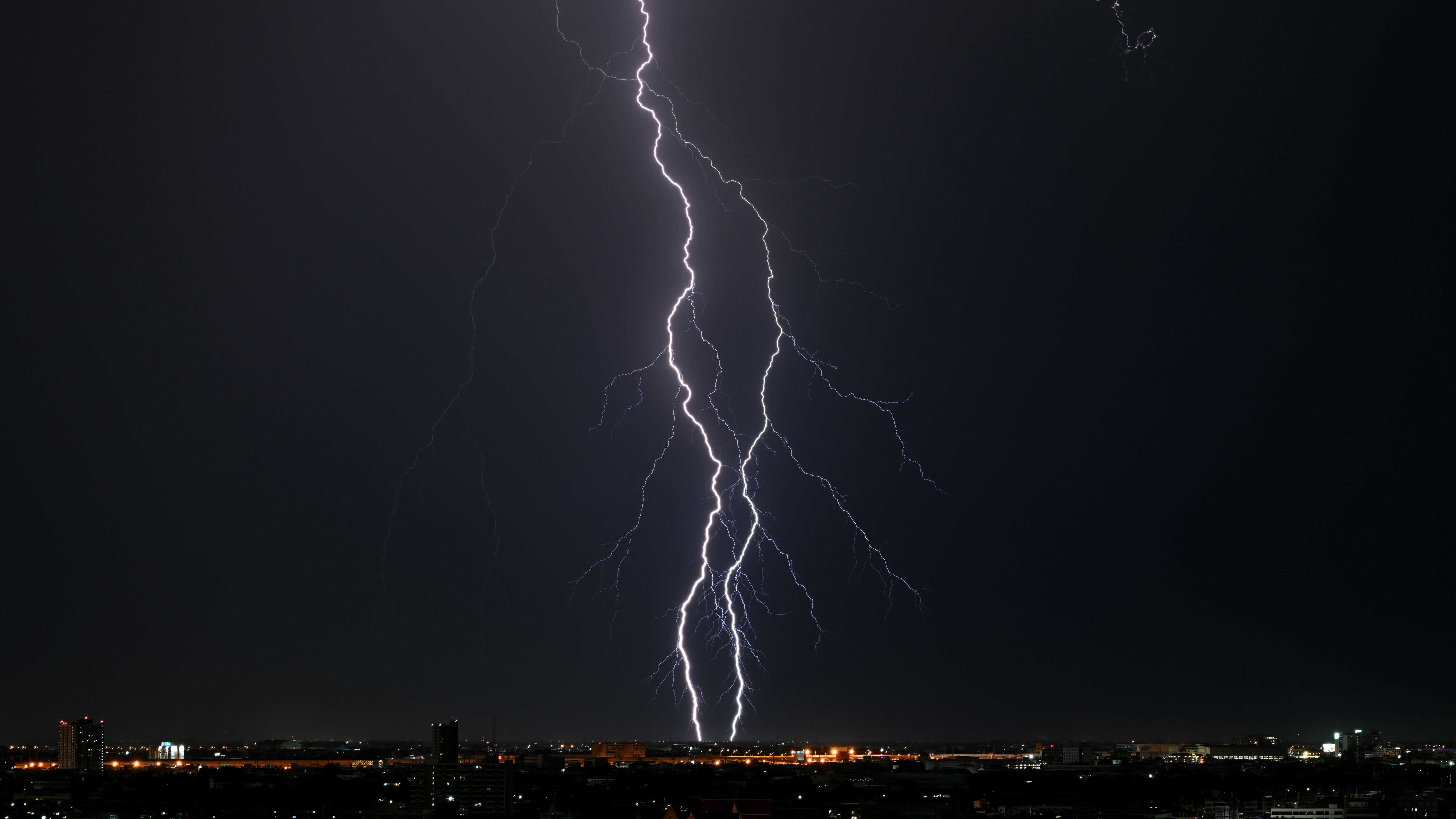 Powerful lightning bolts illuminate the Bangkok skyline as a heavy nocturnal thunderstorm moved in, ending a long period of intense heat. This dramatic weather shift coincides with a fresh warning from the Meteorological Department, predicting heavy to very heavy rain across Thailand from May 14 to 18, 2026. Citizens are urged to stay indoors and follow strict safety protocols. Experts emphasize the "30-30 Rule": if thunder is heard within 30 seconds of a flash, find a secure building or car immediately, and stay inside for at least 30 minutes after the final clap of thunder.
